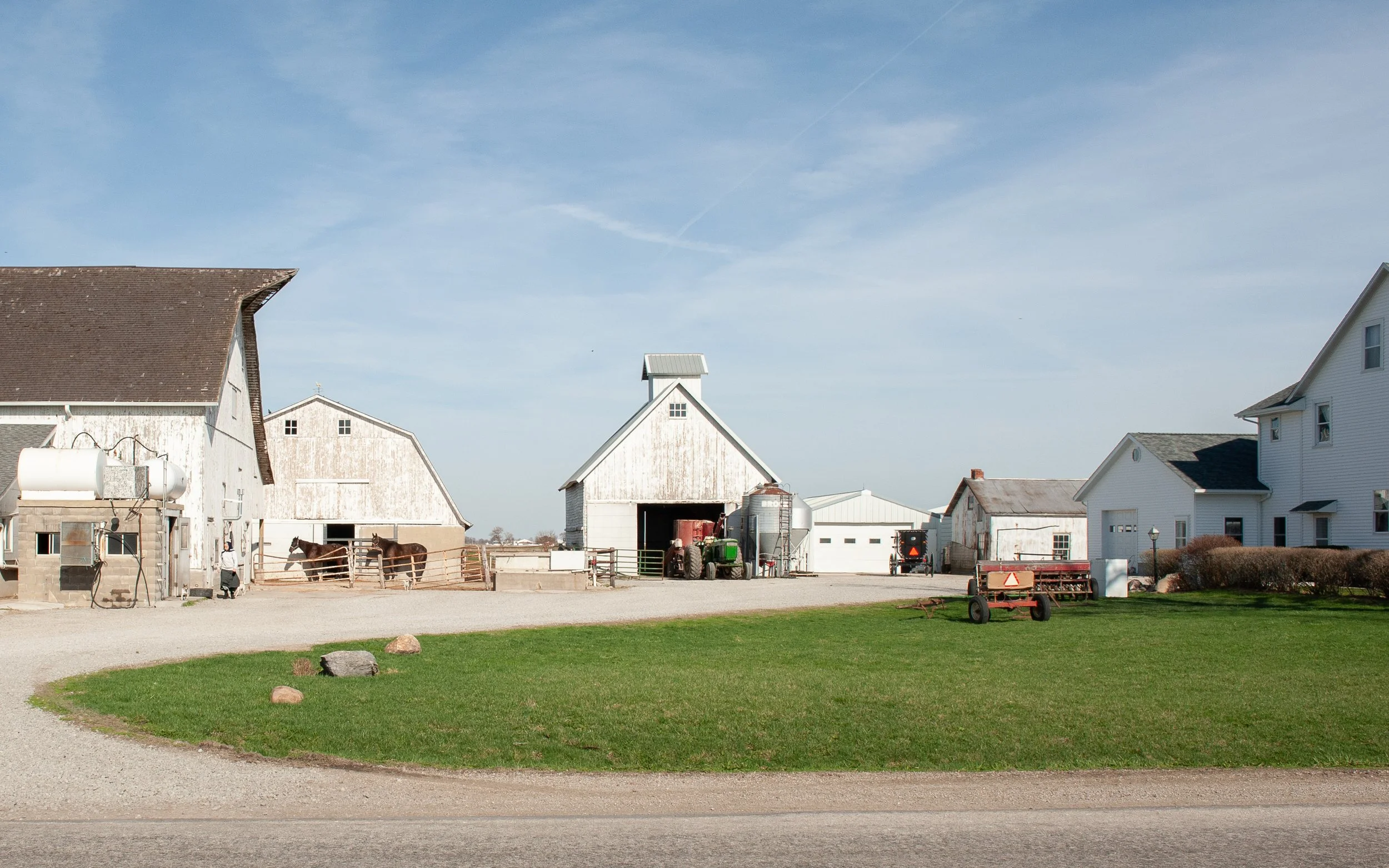 Blick auf einen Bauernhof mit Scheunen, Traktoren, Pferden und Wohnhäusern an einem klaren Tag.