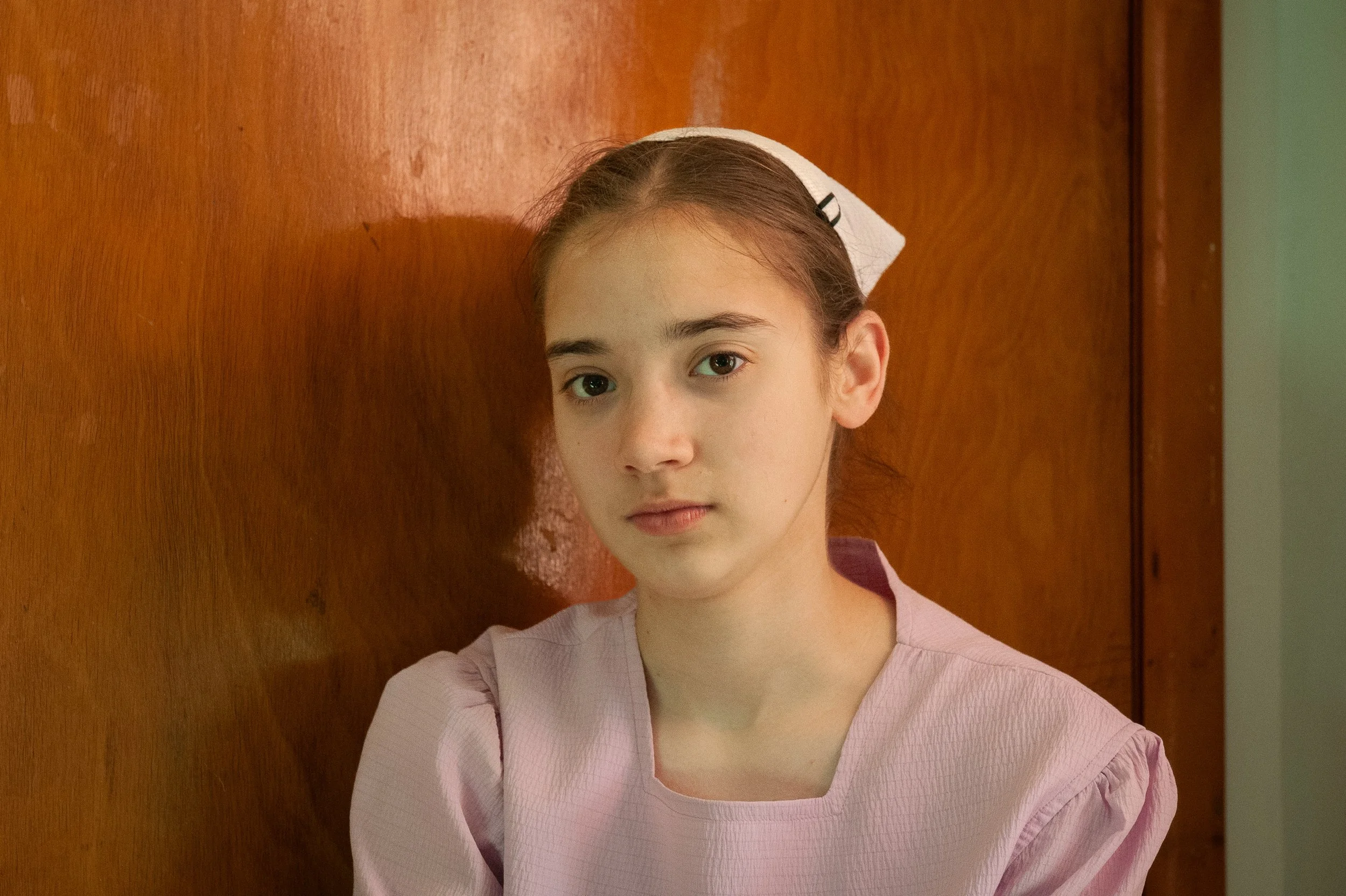 Junge Krankenschwester trägt rosa Uniform und Hausschuh, steht vor Holzwand, blickt in die Kamera.