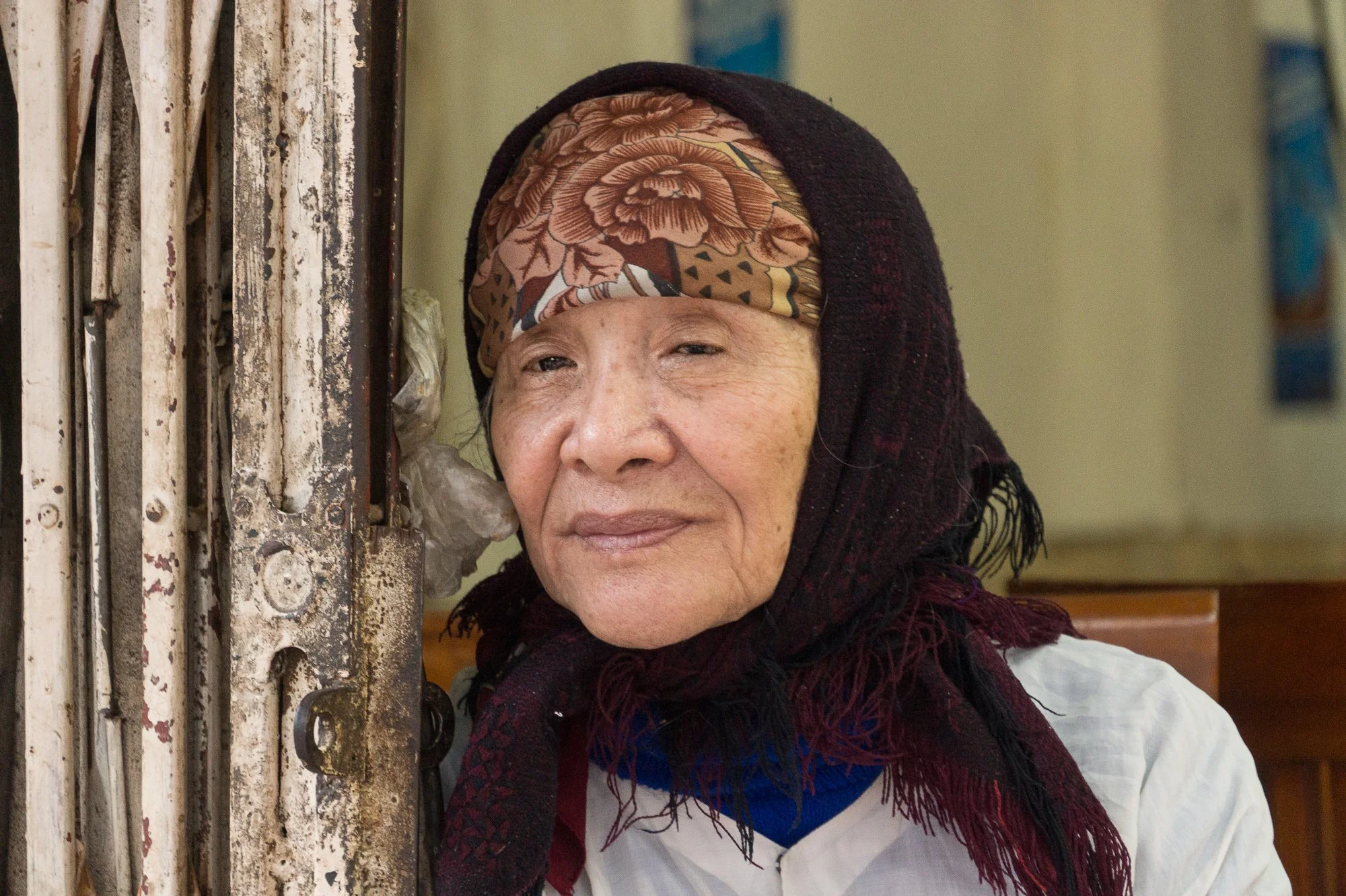 Ältere Frau mit bunter Kopfbedeckung und dunklem Tuch um den Kopf schaut nach links.