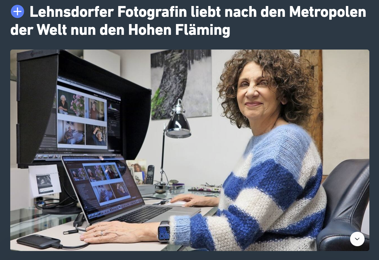 Fotografin arbeitet an einem Computer, bearbeitet Fotos in einer Bildbearbeitungssoftware, in einem Büro mit Wanddekorationen im Hintergrund.