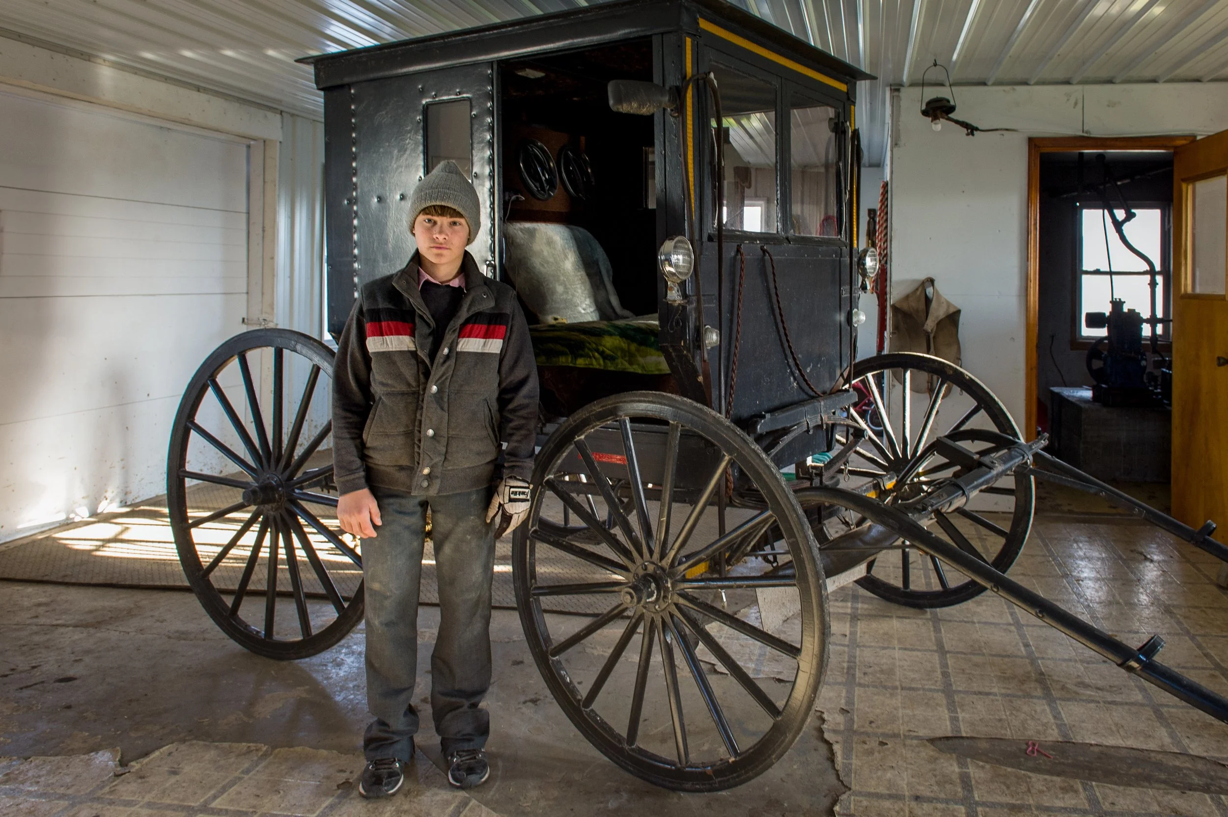Junge steht neben einer antiken Kutsche in einem Raum mit Holzboden und Metallwänden.
