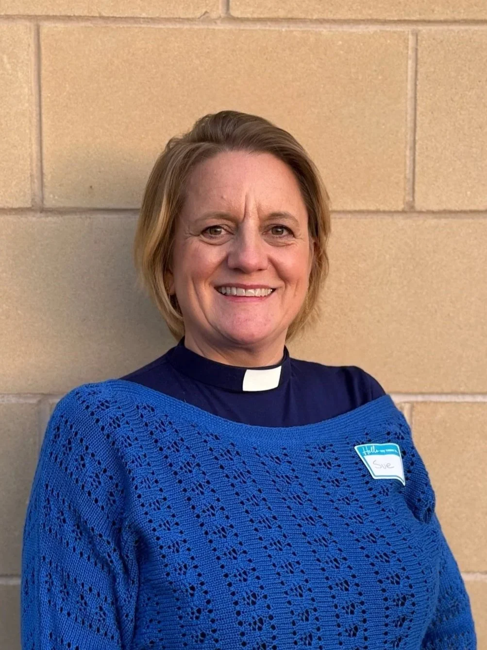 A woman dressed as a priest inside a church, smiling at the camera.