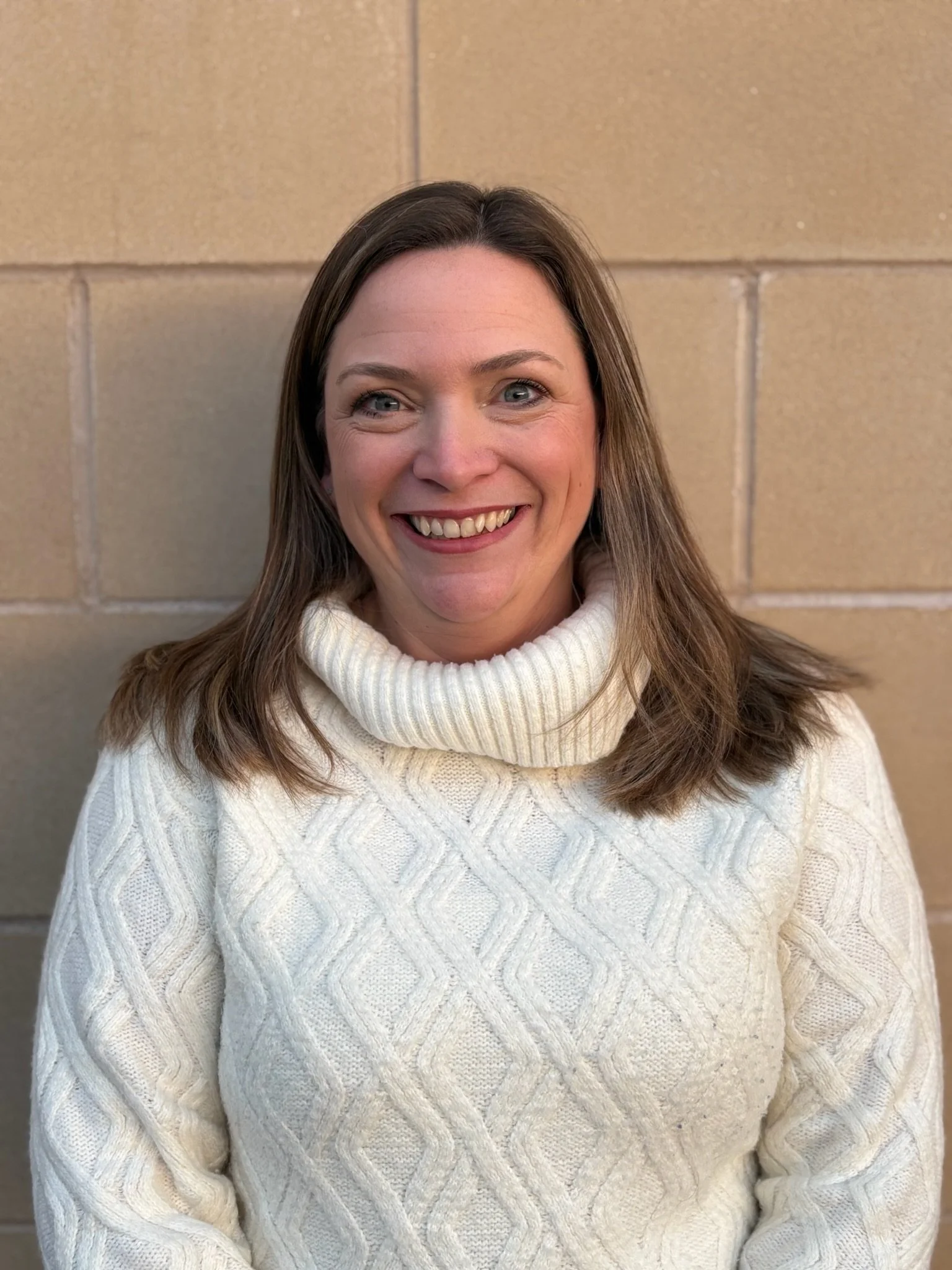 Portrait of a woman with curly hair wearing a teal top and black blazer, smiling in front of a plain background.