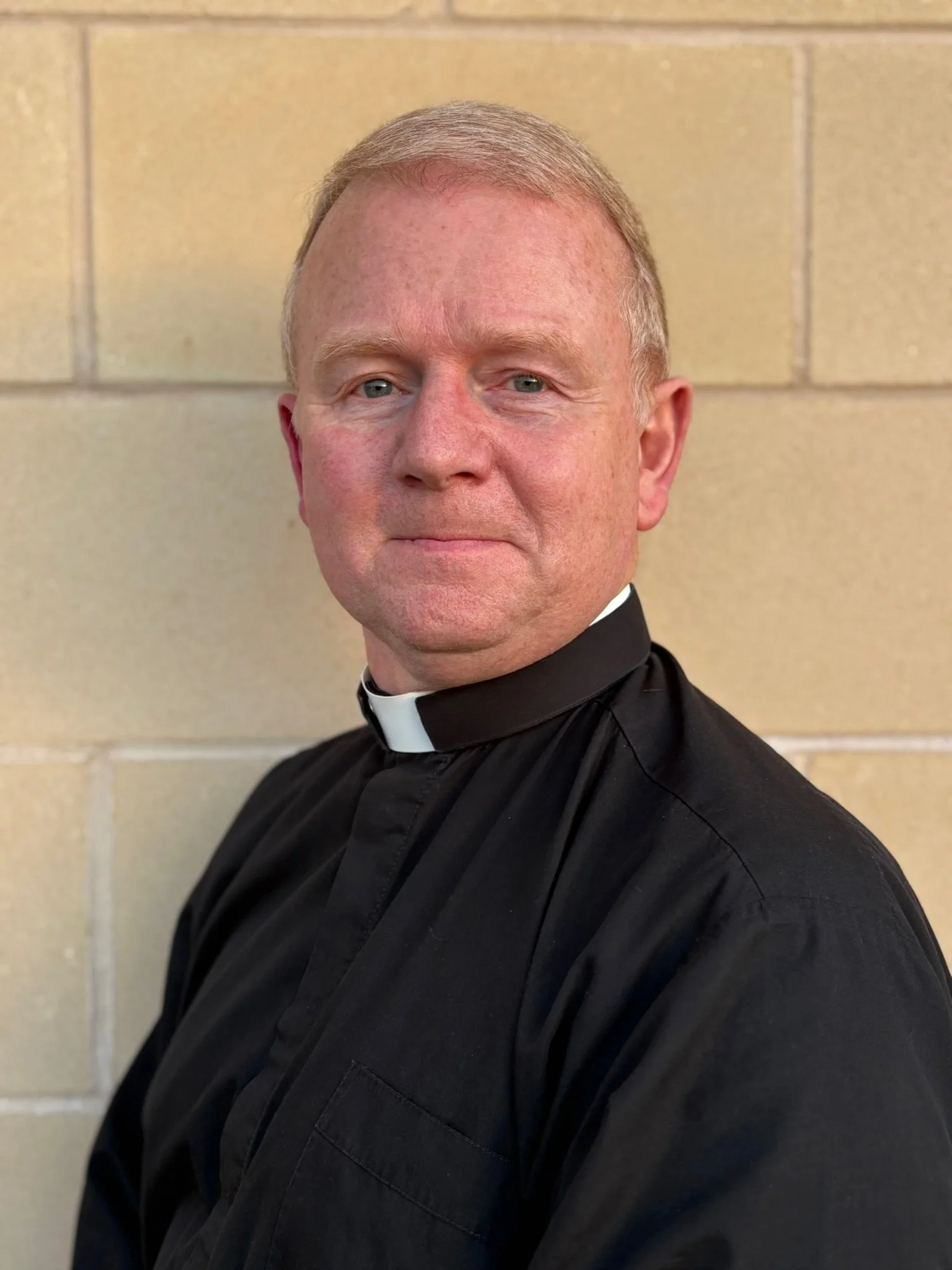 A woman dressed as a priest inside a church, smiling at the camera.