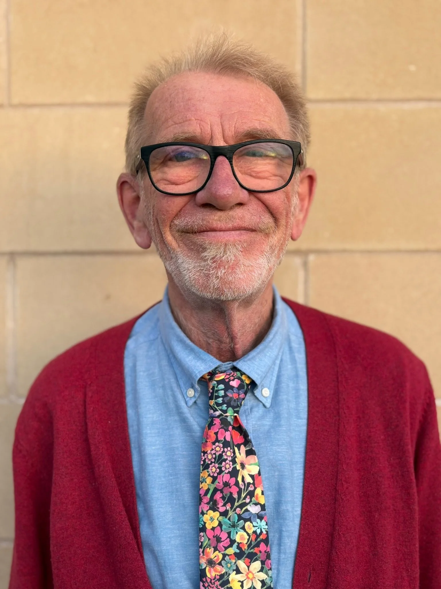 Portrait of a woman with curly hair wearing a teal top and black blazer, smiling in front of a plain background.