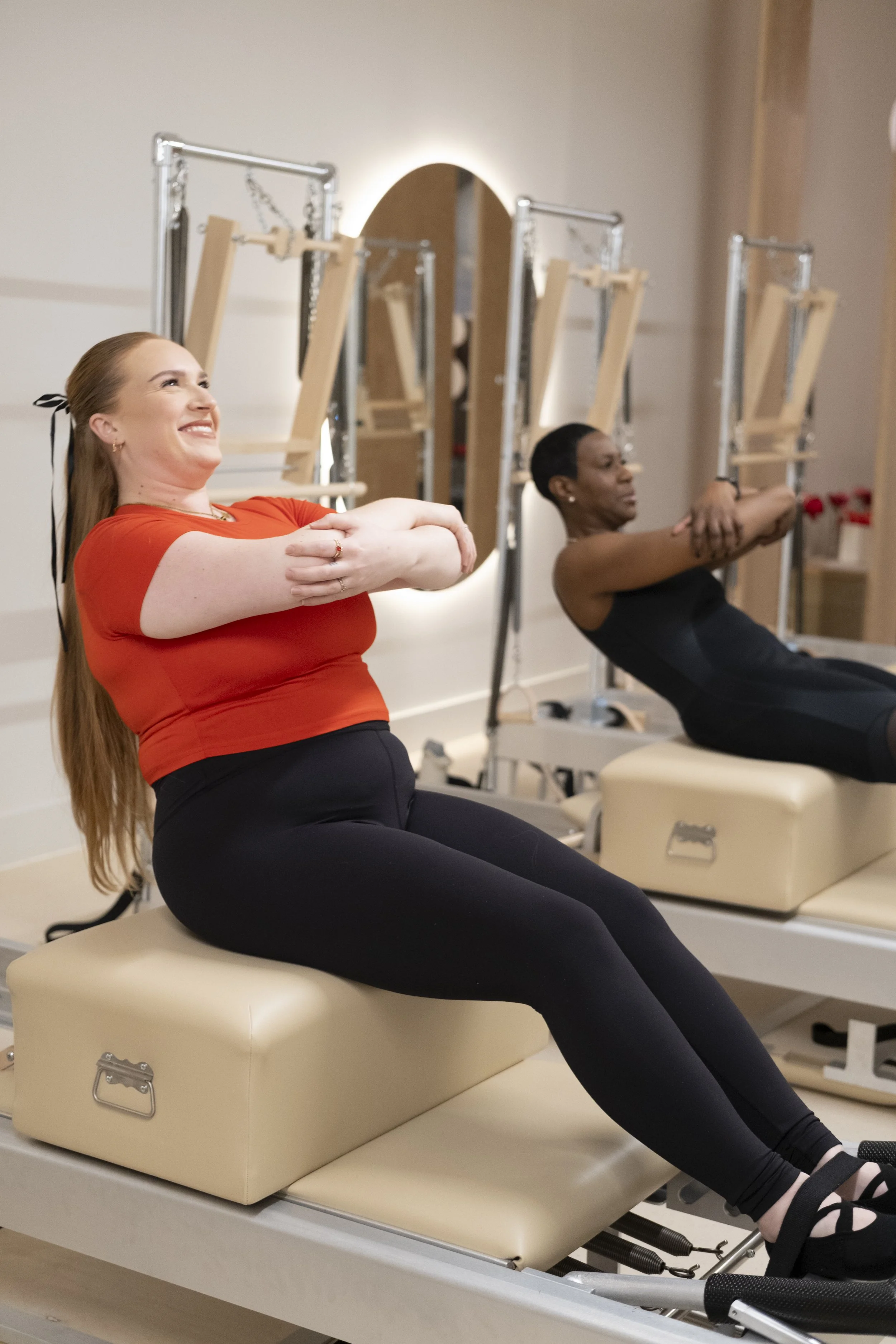 Two women performing Pilates exercises on reformer machines in a fitness studio.
