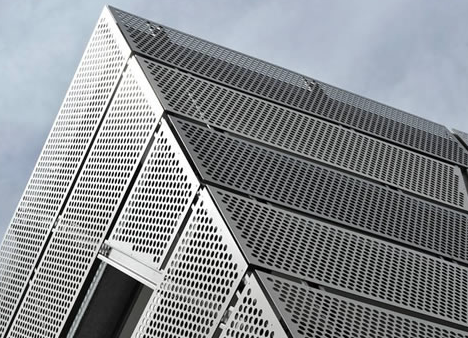Close-up of a modern high-rise building with a perforated metal facade and angled architecturally distinctive design.