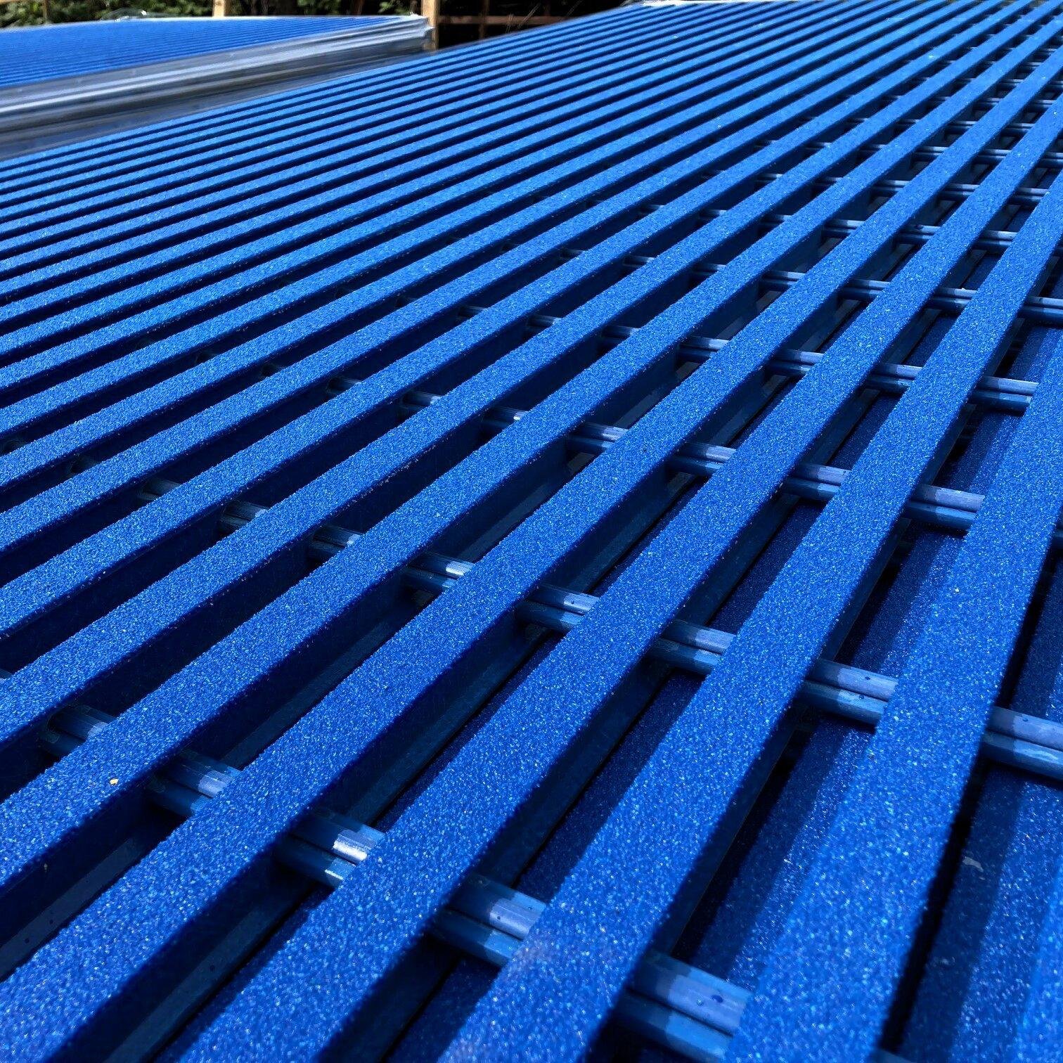 Close-up view of a blue outdoor playground surface made of textured rubber strips with a grid pattern.