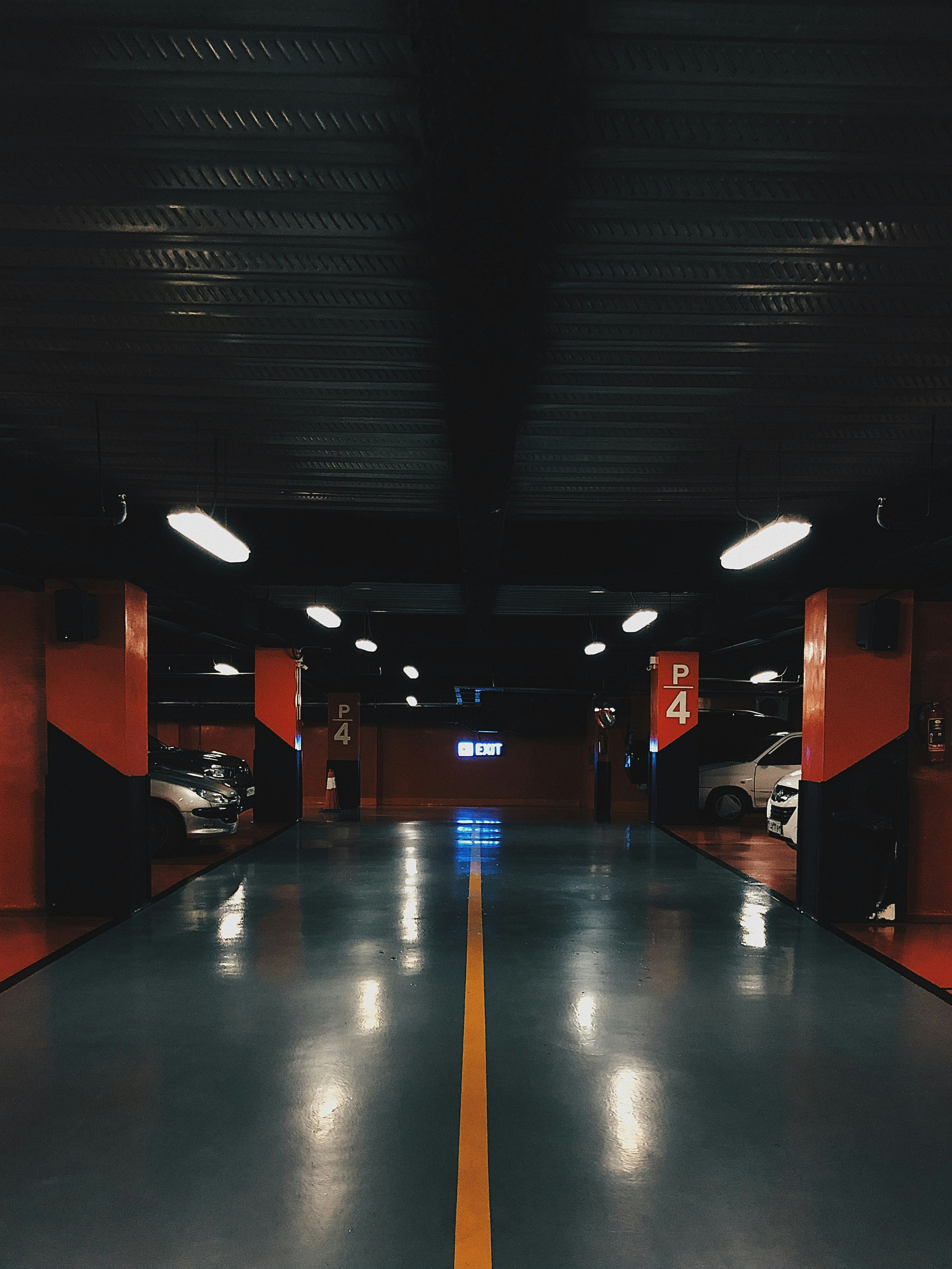 Underground parking garage with parked cars on either side, overhead lights, and an illuminated exit sign in the background.