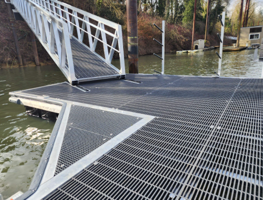 A metal dock with a roller ramp extending into the water, surrounded by trees and boat docks.