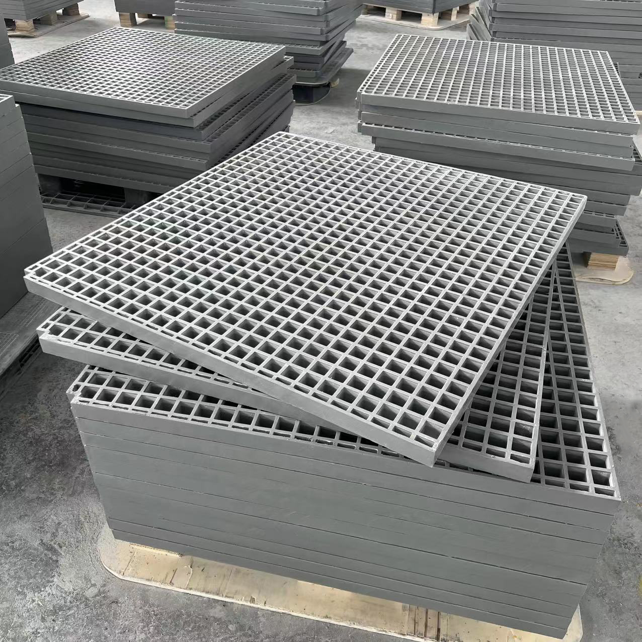 Stacks of gray metal grates and panels stored on pallets in an industrial warehouse.