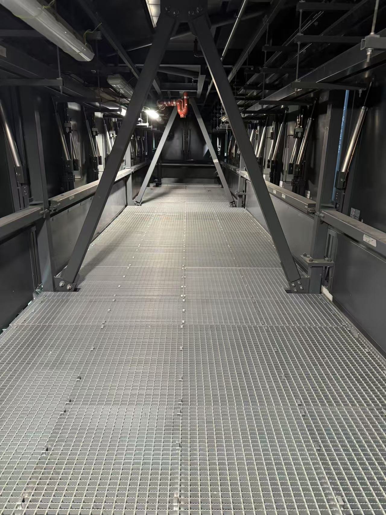 Empty industrial platform with metal grating floor inside a black-finished mechanical or server room with supporting beams and piping.