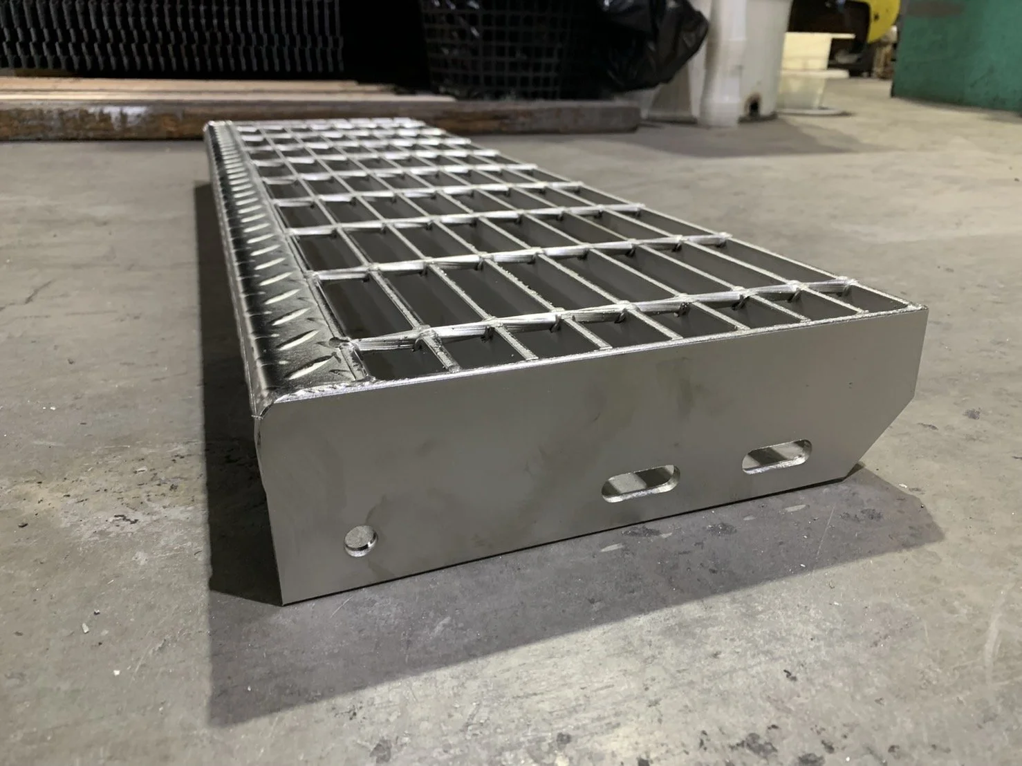 A rectangular metal grate with a grid of squares, placed on a concrete floor in an industrial setting.