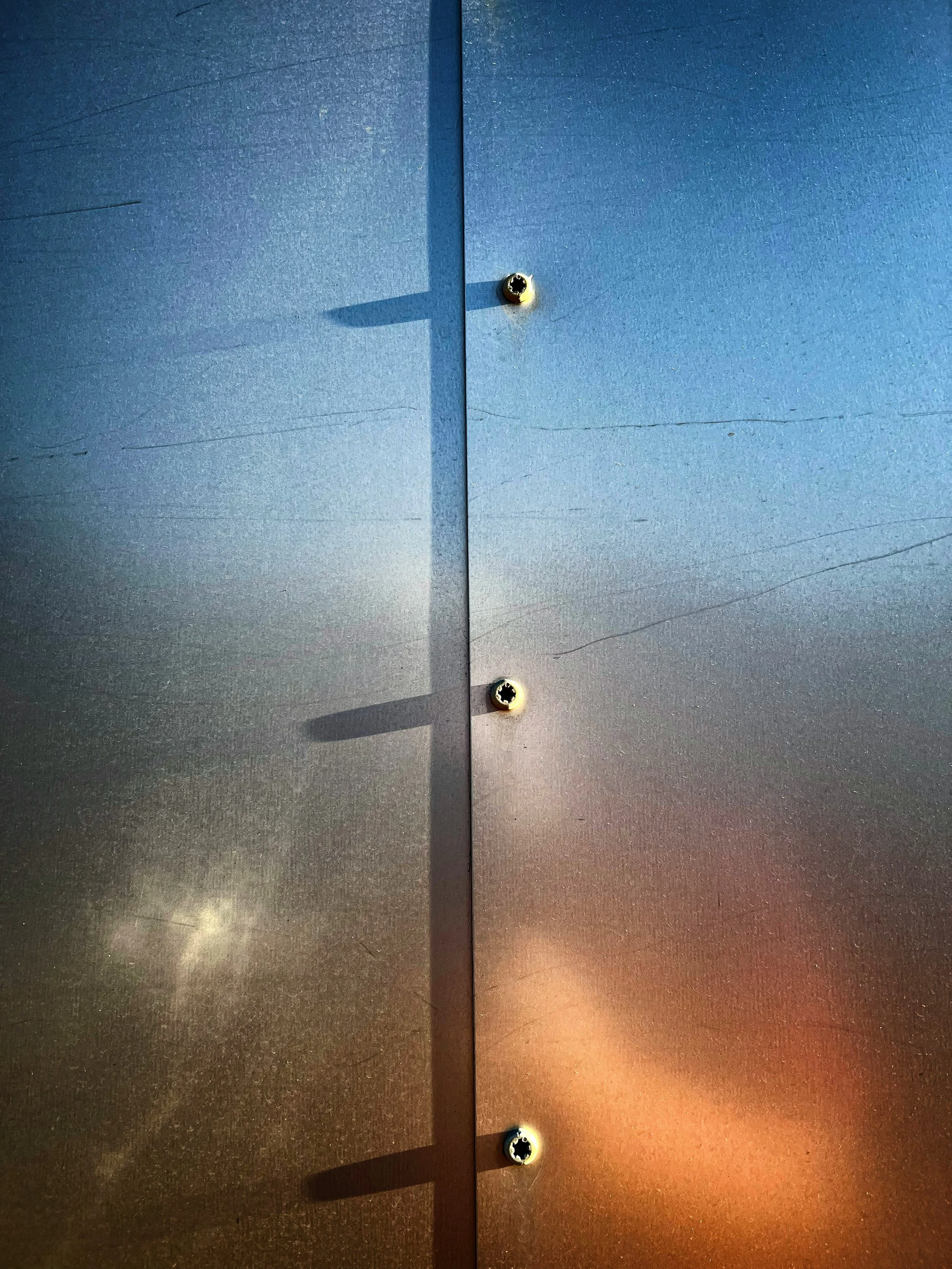 Close-up of a metallic surface with three visible screws, creating shadows on the surface.