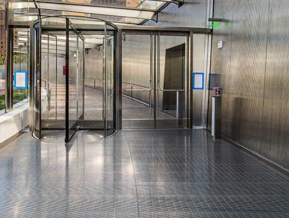Indoor area with a revolving glass door, an automatic door, metal walls, and a fire alarm on the wall.