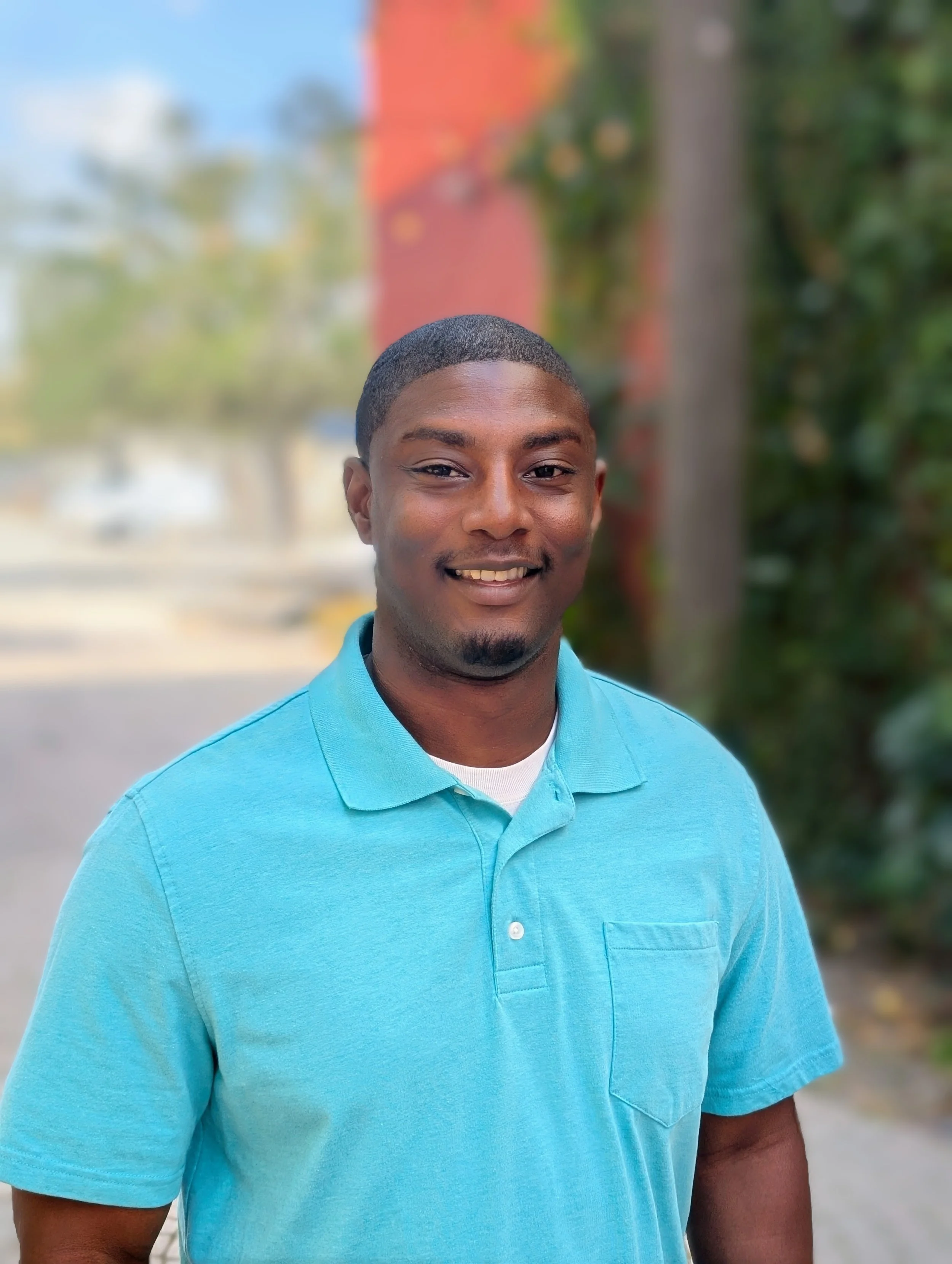 A smiling young man in a turquoise polo shirt standing outdoors  | Professional Organizer and Life Coach | Household Stewardship LLC
