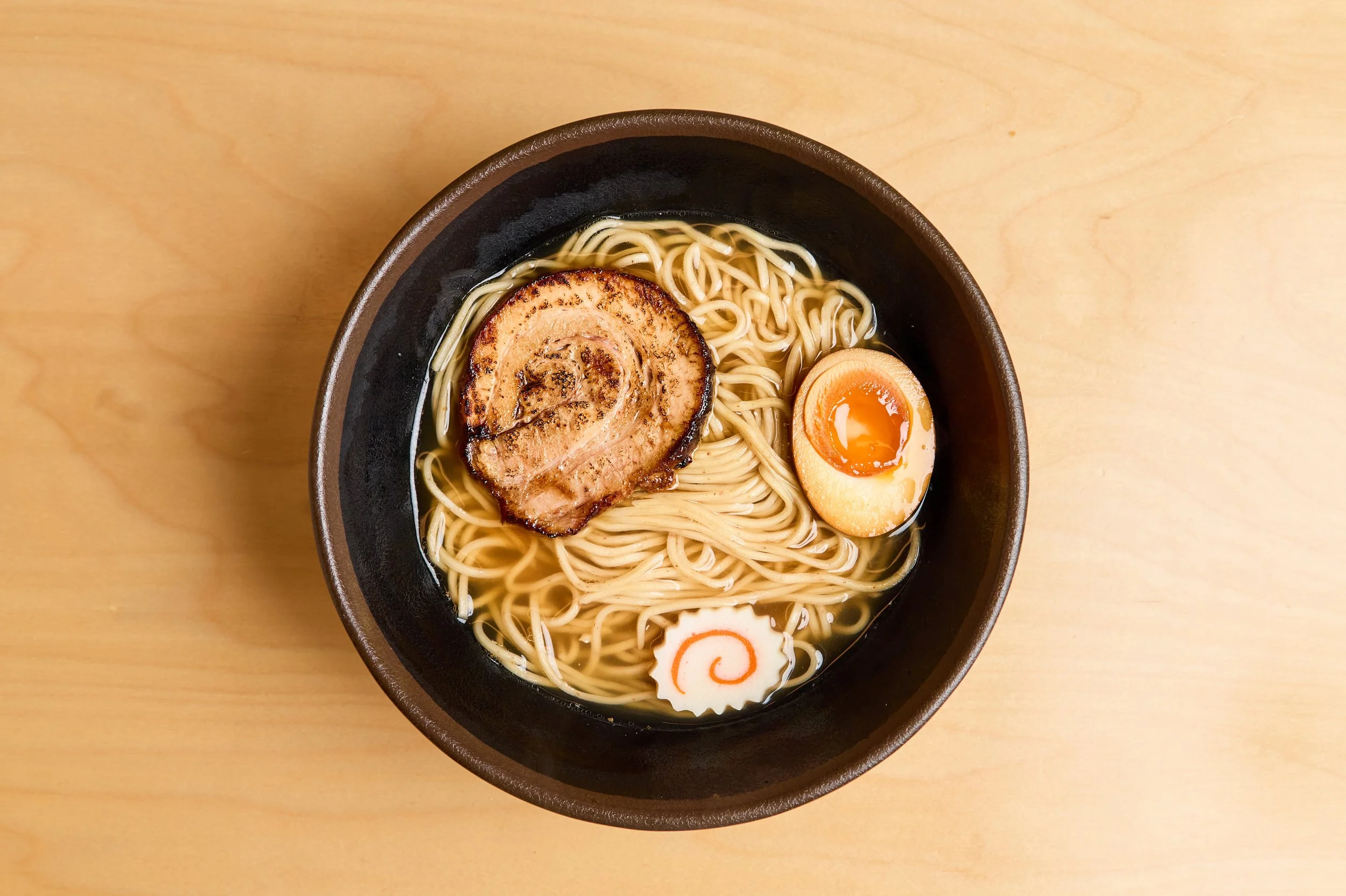 Tigela de ramen com chashu de porco, ovo marinado com gema mole, naruto, e macarrão em caldo claro.