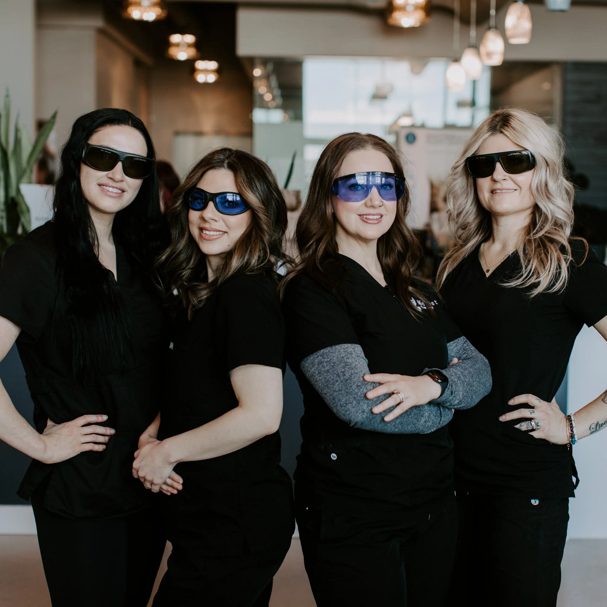Four women wearing black uniforms and sunglasses standing indoors.