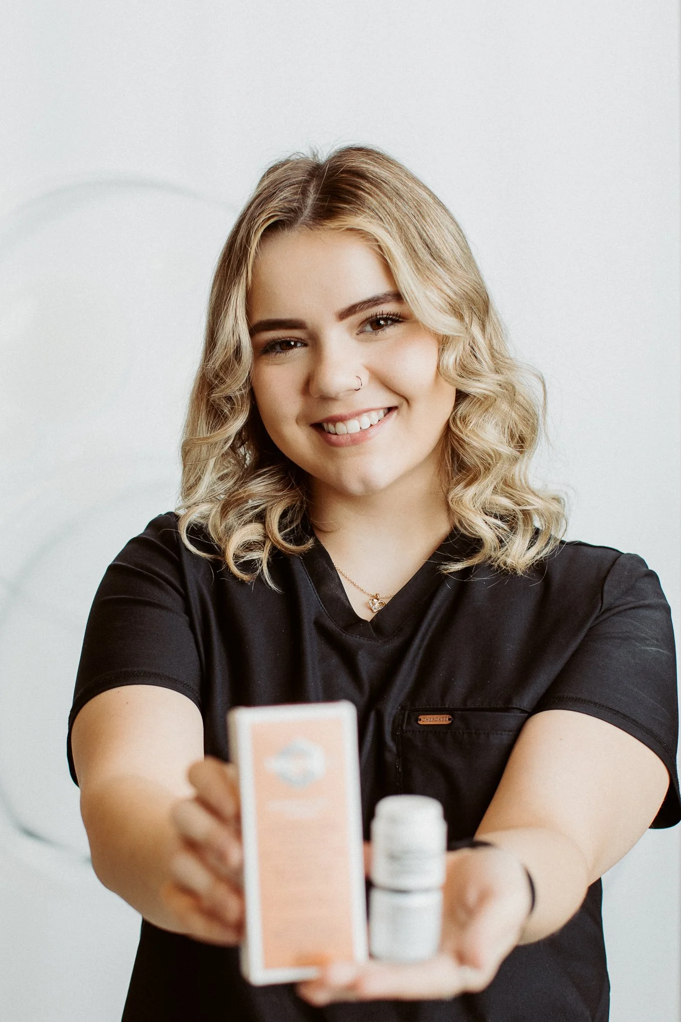 A woman smiling and taking a selfie with a phone, with health and supplement bottles on a table in front of her.