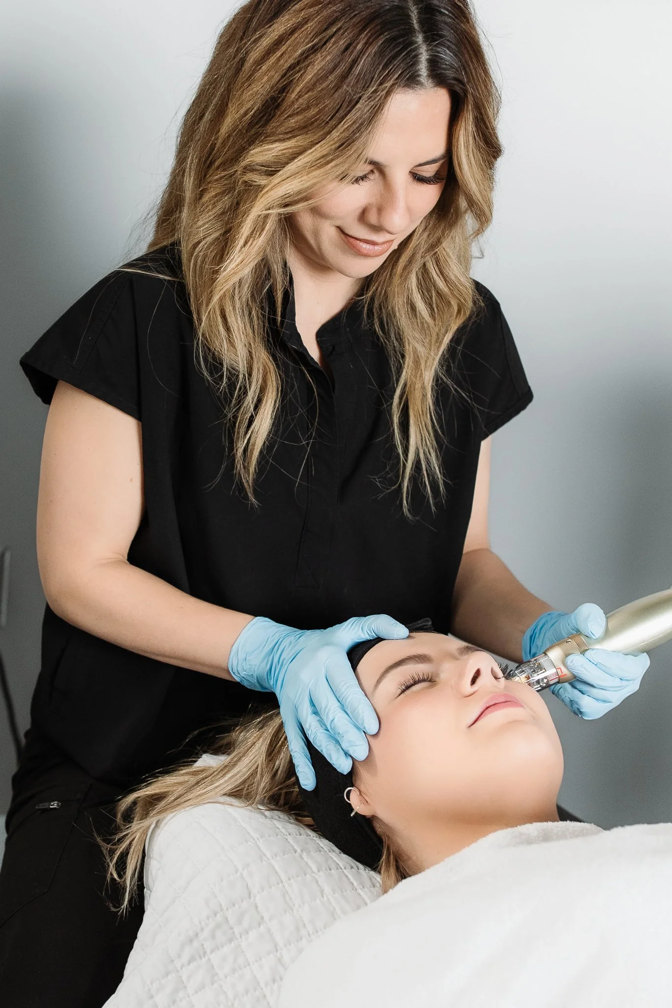 A woman lying on a treatment bed receiving a facial treatment with a device from a professional wearing gloves.