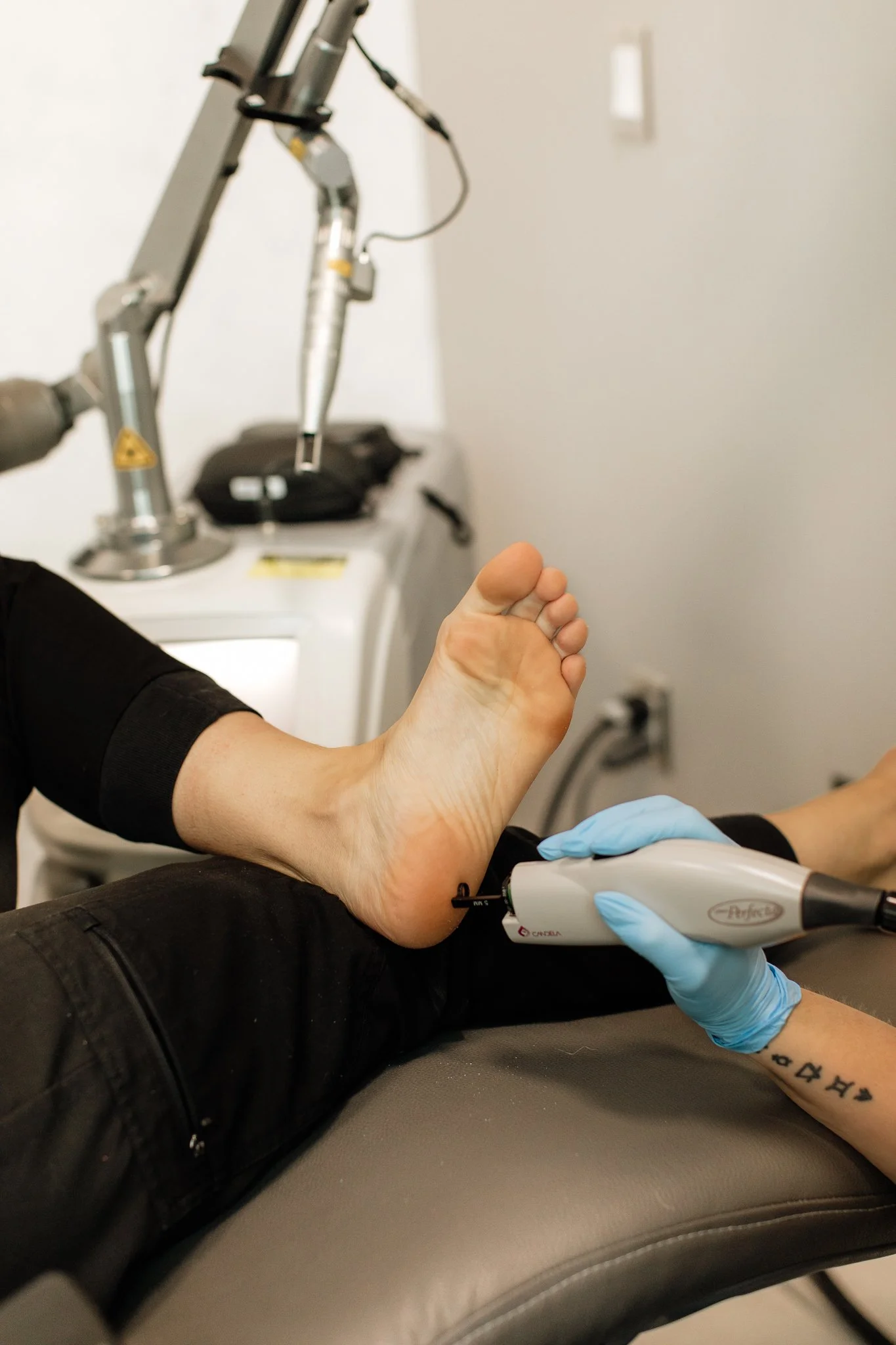 A person receiving a tattoo on their ankle using a tattoo machine, with a tattoo artist wearing blue gloves.