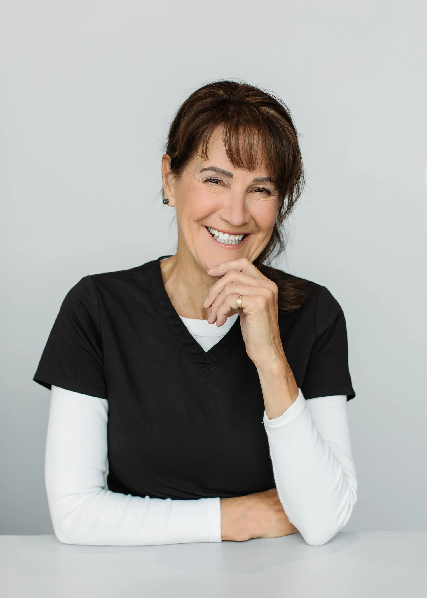 Smiling middle-aged woman in black medical scrubs posing with her hand under her chin