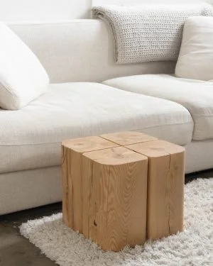 A white sofa with pillows and a wooden cube side table on a white rug.