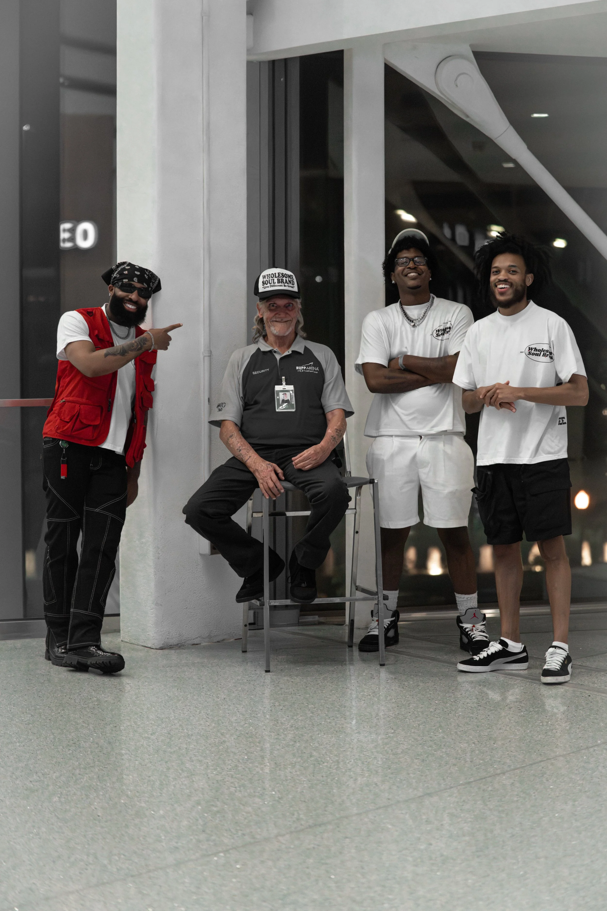 Four men standing indoors, one seated on a stool, casually dressed, smiling and posing for a photo at night.