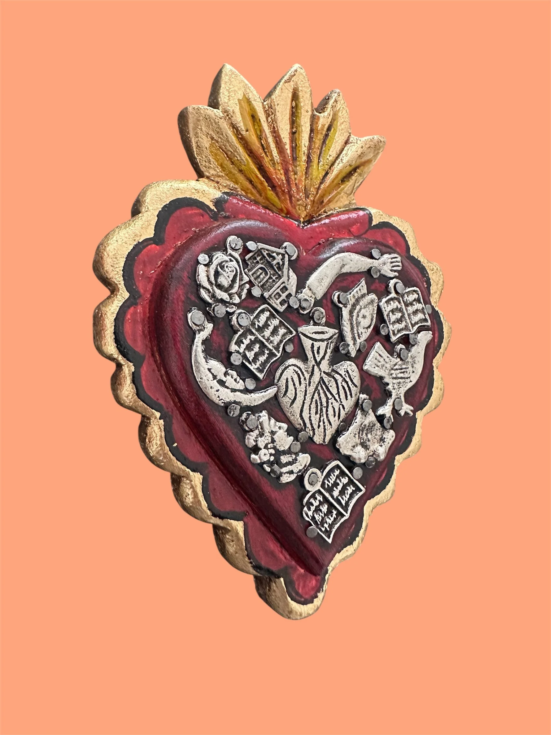 Close-up detail of extra large gold and red Mexican milagrito heart with traditional folk art design.