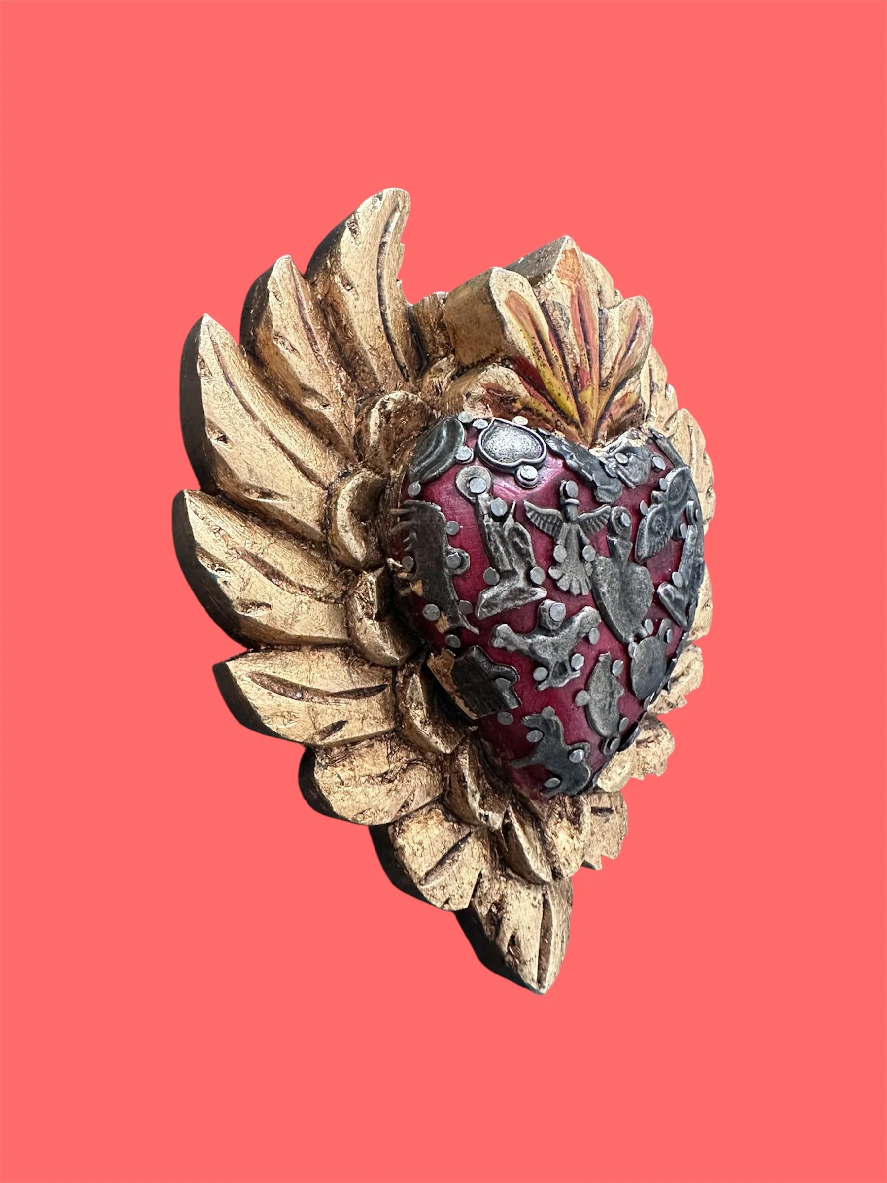 Close-up detail of Mexican milagrito heart with wooden wings featuring traditional folk art design.