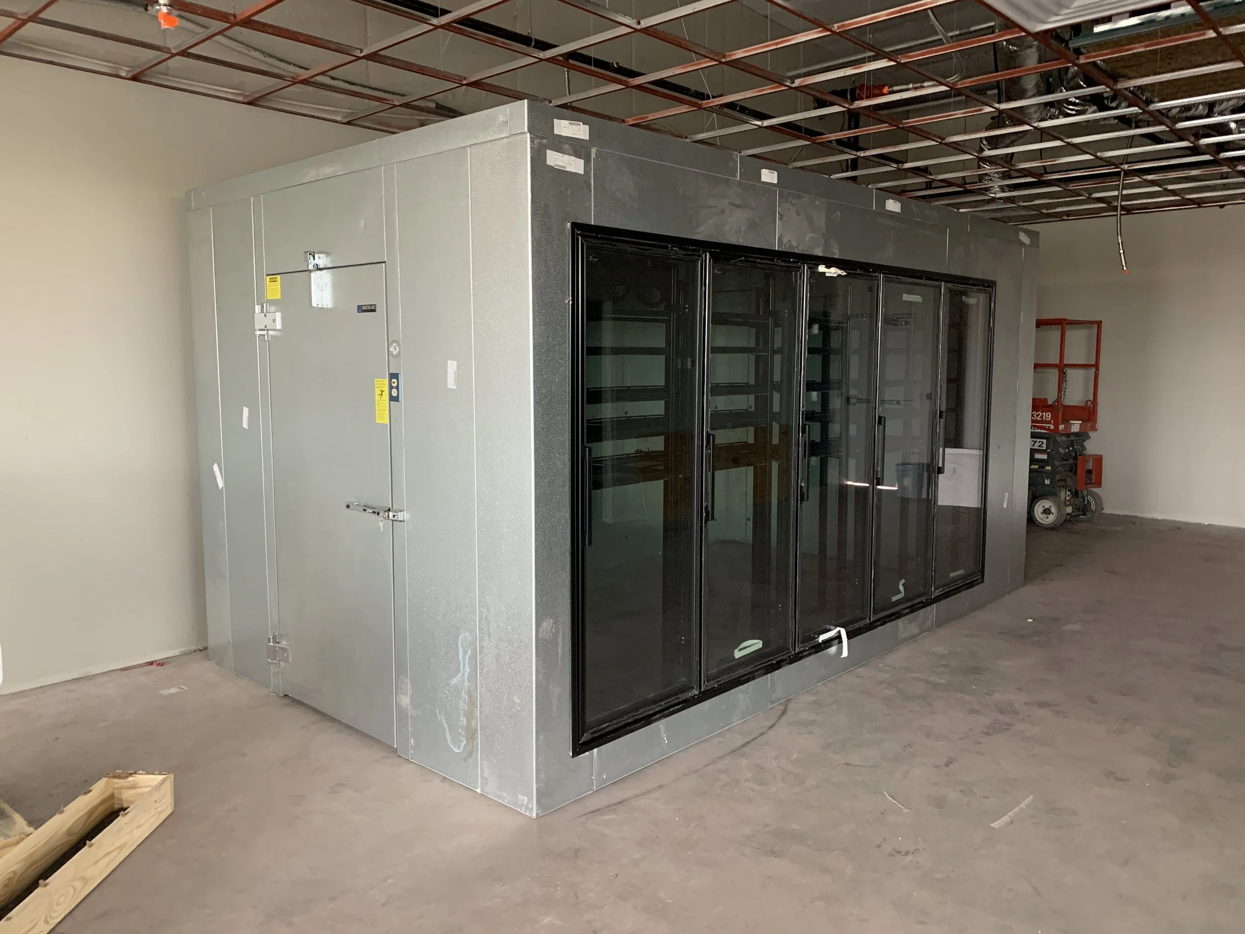 Cooler enclosure and multi-door case set and leveled with utility rough-ins complete.