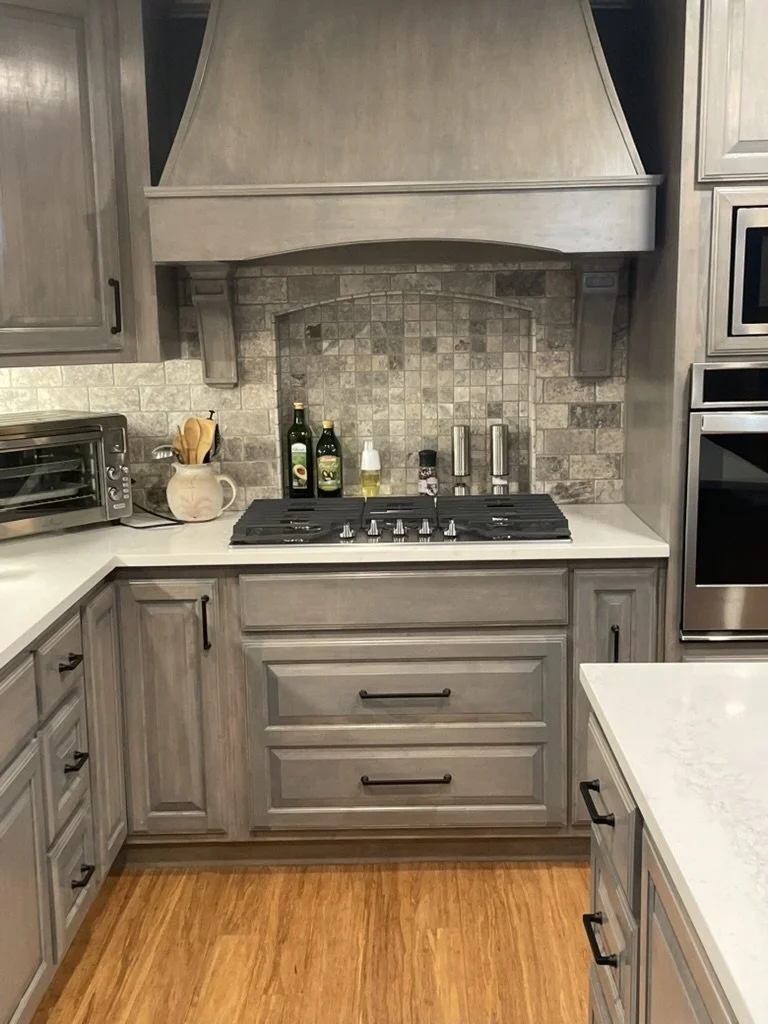 Custom hood and textured stone backsplash frame the cooktop with coordinated hardware and lighting.