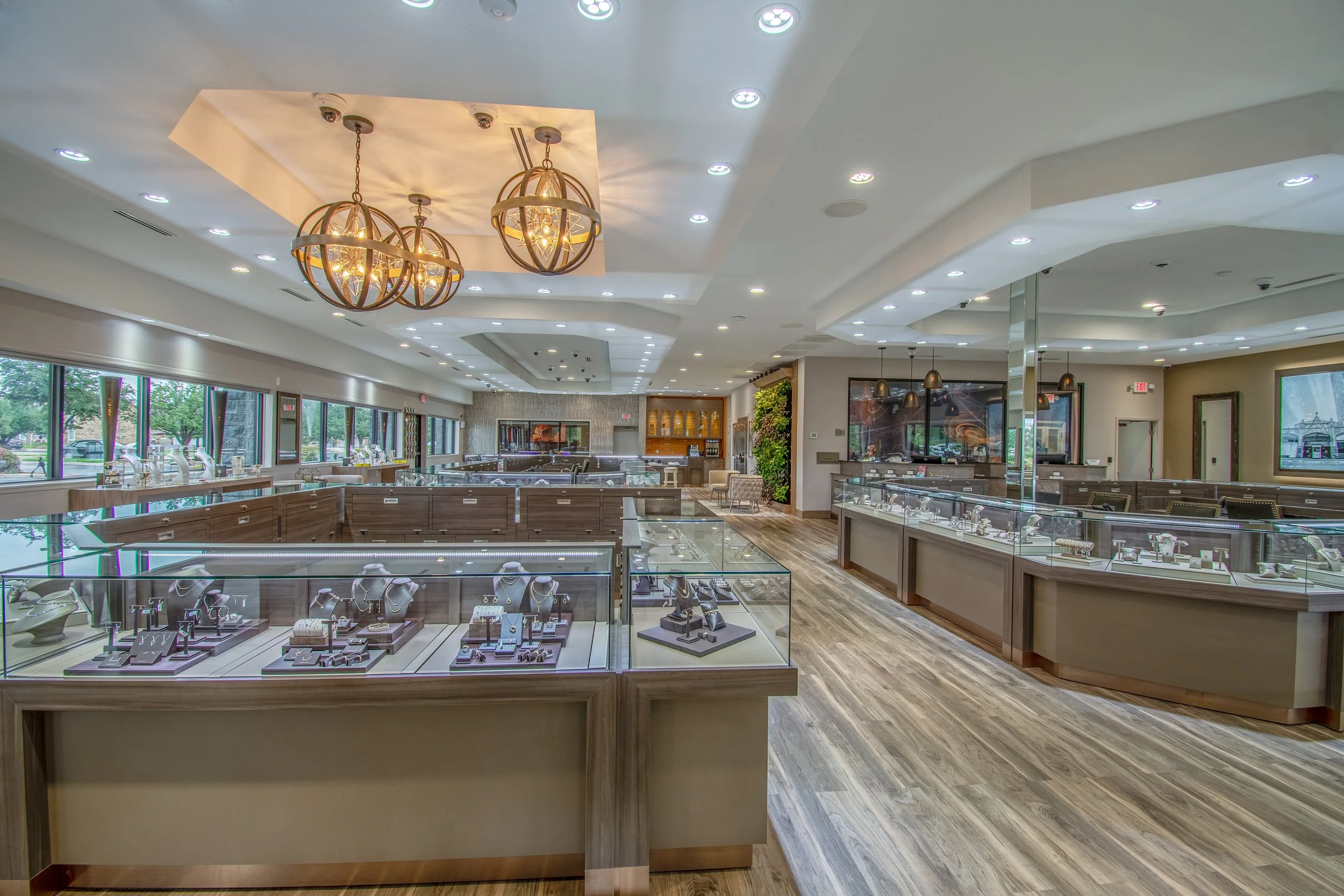 Expanded jewelry showroom with glass islands wood flooring and statement lighting.