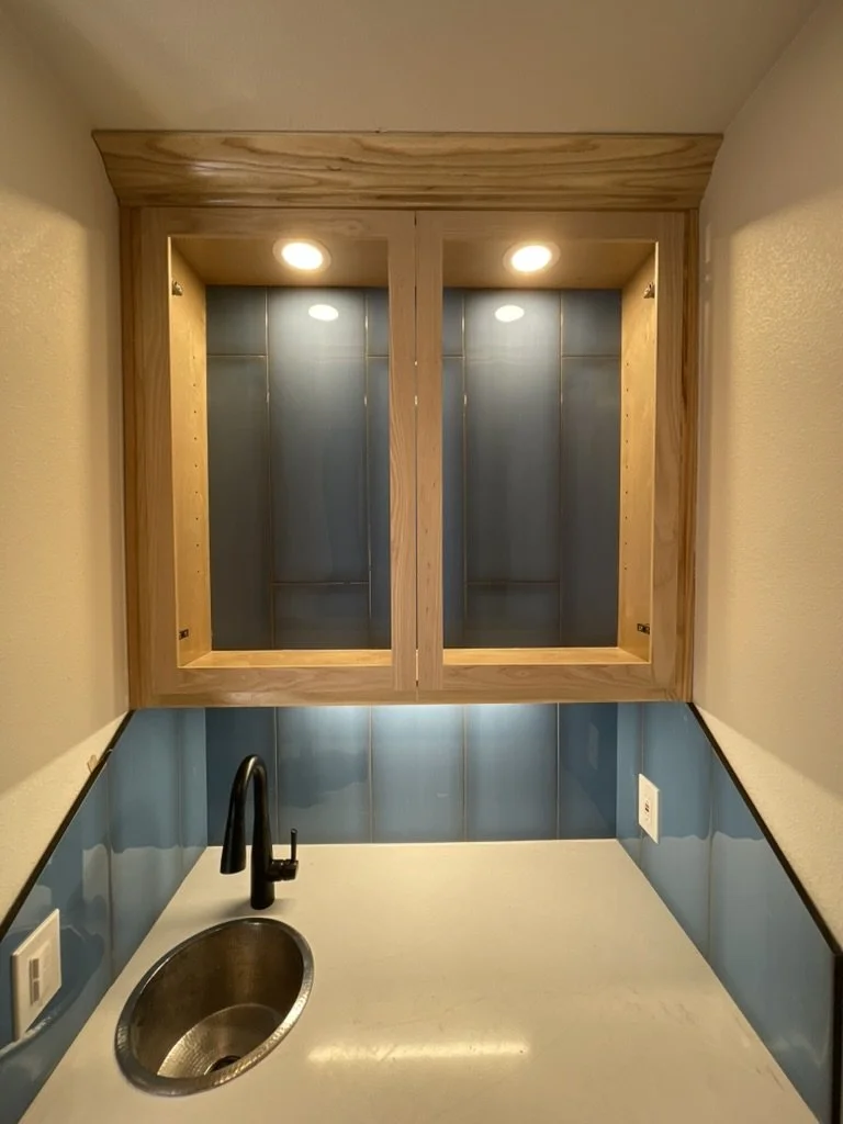 Lighted display cabinet and glass tile create a clean bar nook with a black faucet set.