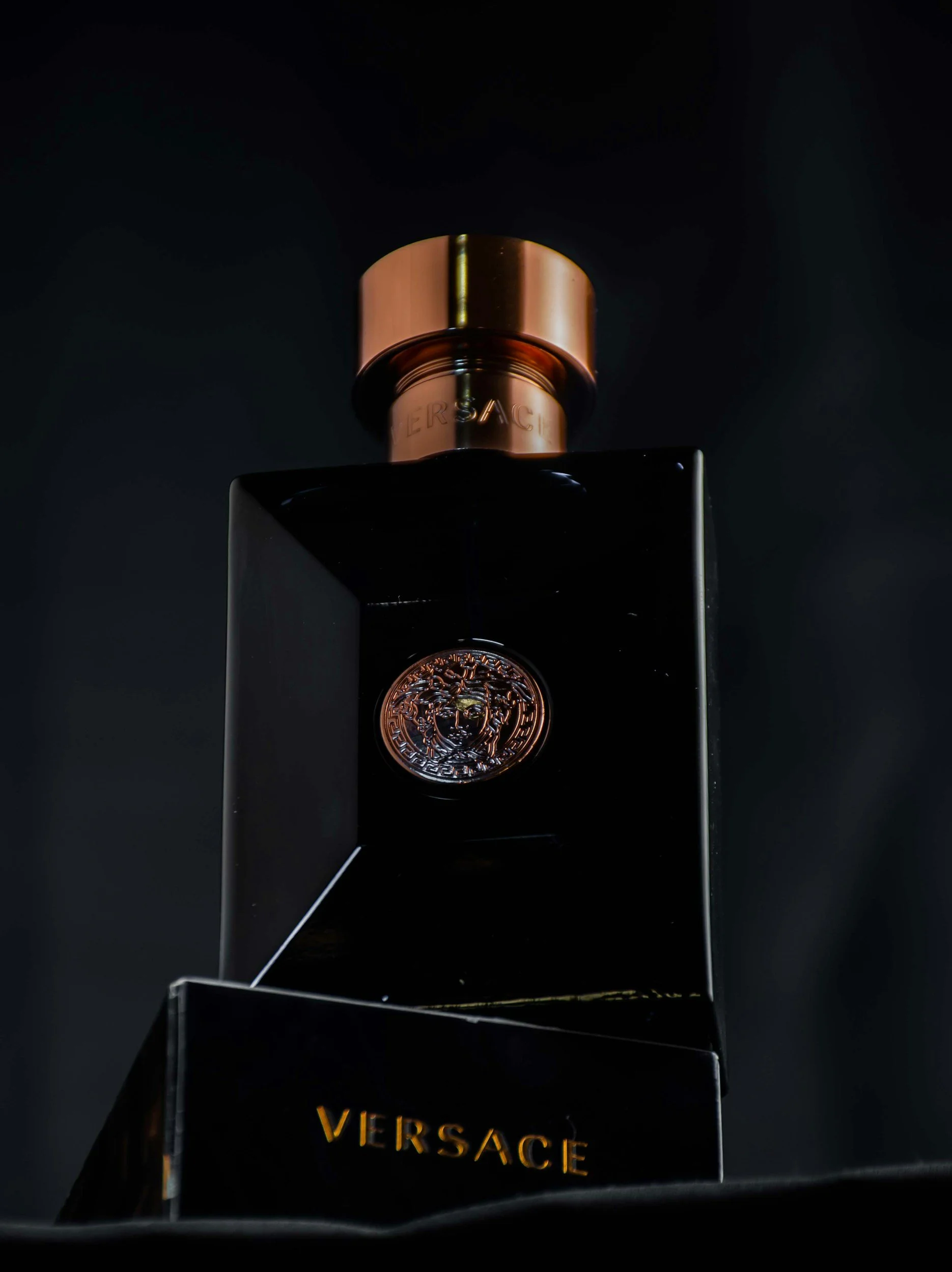 A black bottle of Versace perfume with a gold cap, displayed on a dark surface.