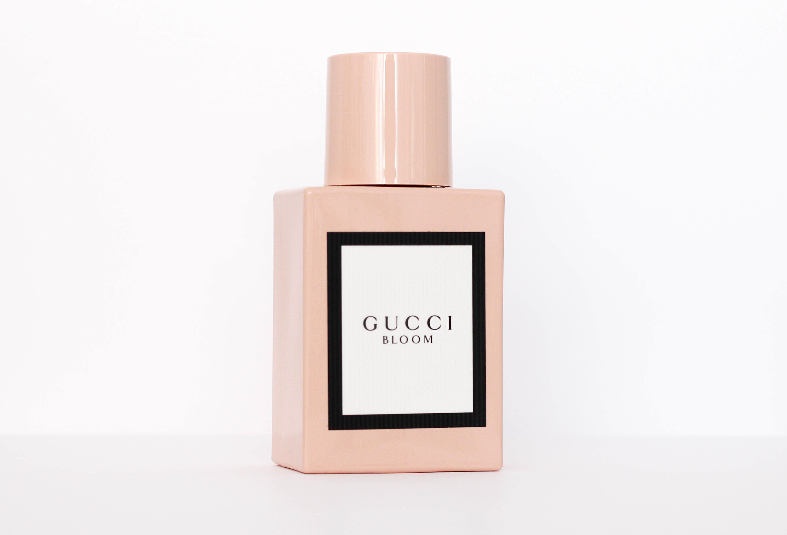 A pink Gucci Bloom perfume bottle with a black and white label on a white background.