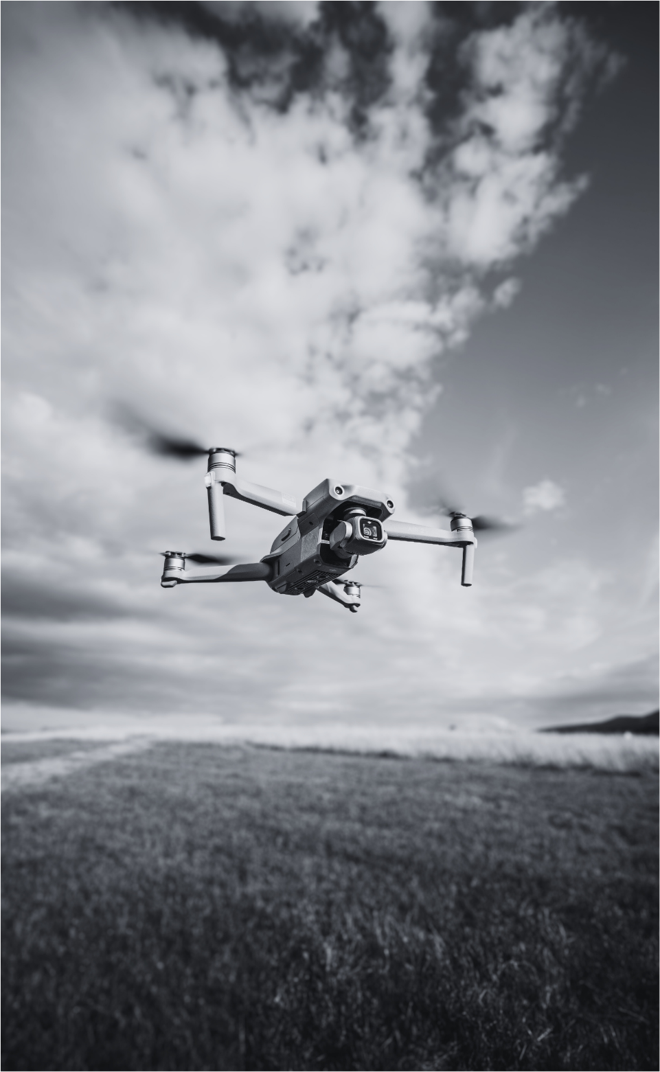 A drone flying over a landscape with grass and hills, under a partly cloudy sky.