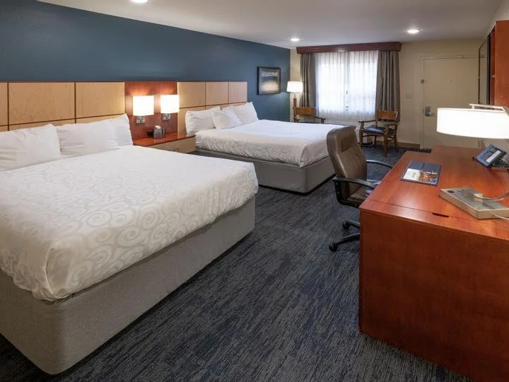 Hotel room with two queen beds, a wooden desk with a telephone, a chair, and window with curtains.