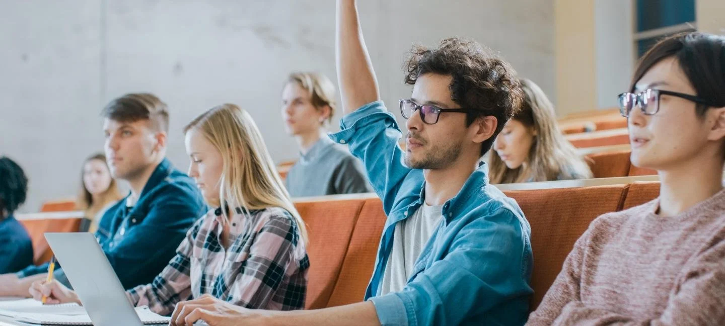 Students in a lecture hall, one raising their hand.
