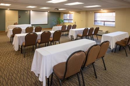 Empty conference room with tables covered in white tablecloths and brown chairs, a blackboard, and windows with blinds.