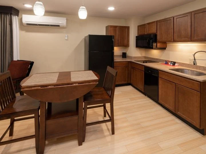 Kitchen and dining area with wooden table, chairs, black refrigerator, microwave, and wooden cabinets.