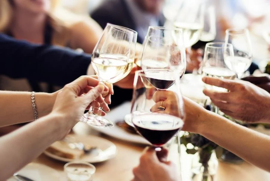 Multiple people clinking glasses of white and red wine during a social gathering.