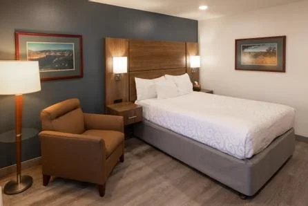 Hotel room with a king-sized bed, brown armchair, two wall-mounted lights, and framed artwork on the walls.