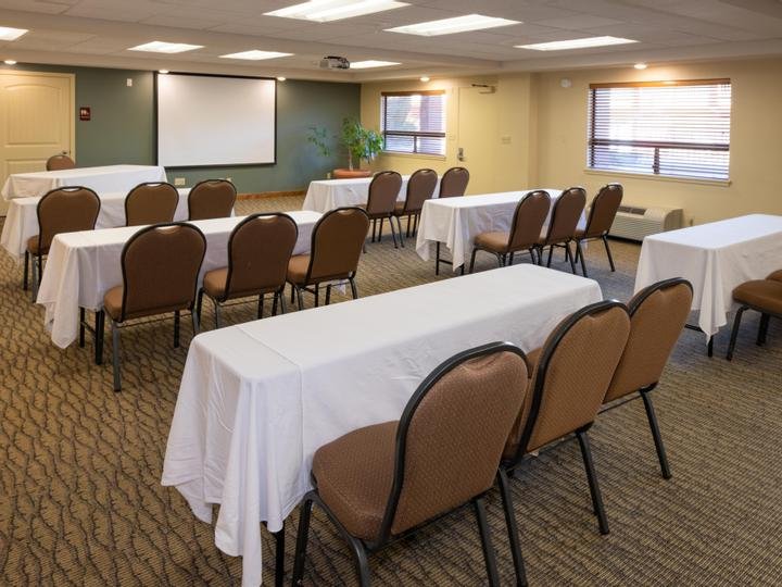 Empty conference room with tables covered in white cloth, brown chairs, a whiteboard, and windows with blinds.
