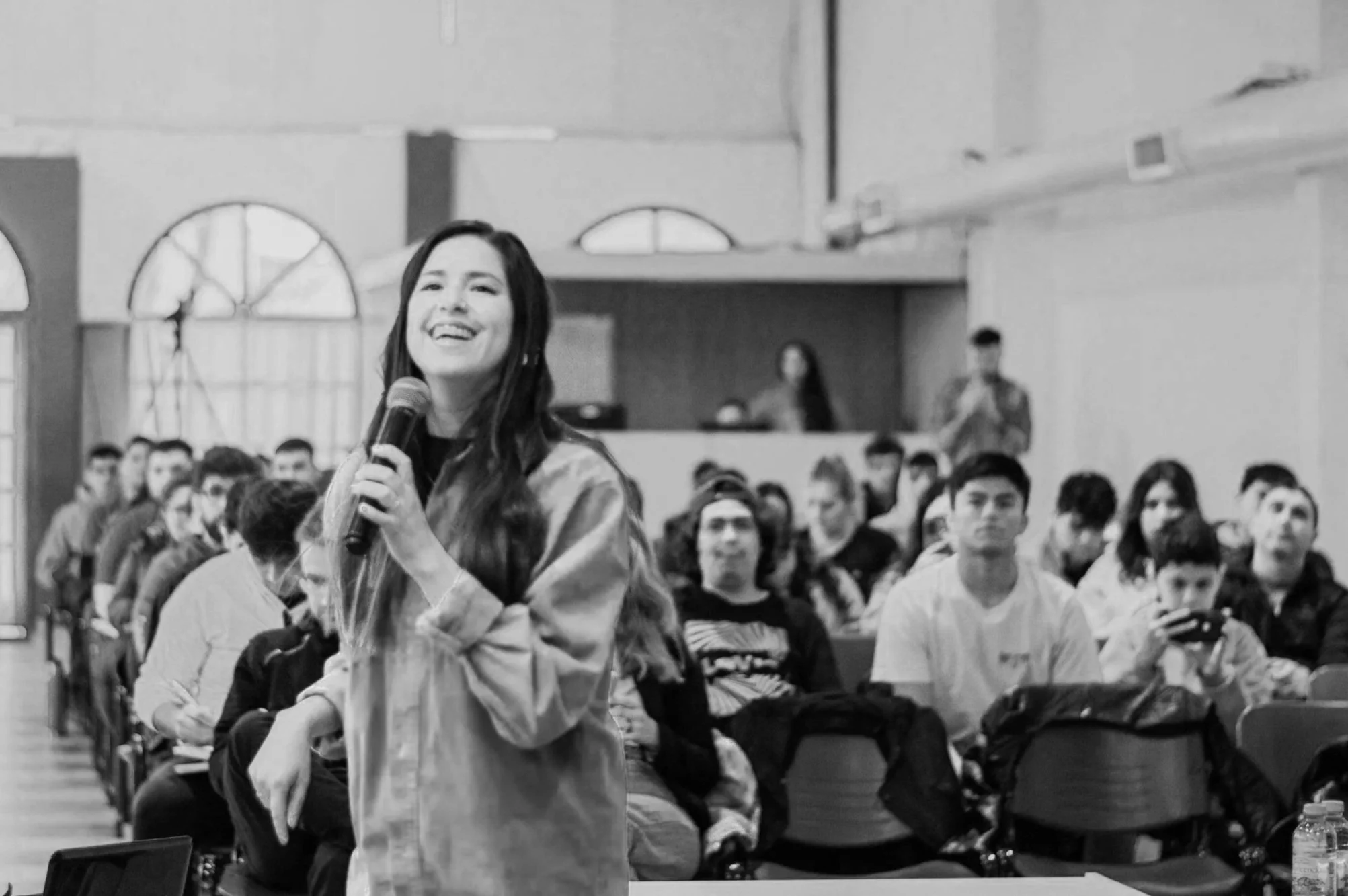 Juvenil mujer con micrófono en un auditorio lleno de jóvenes asistentes.