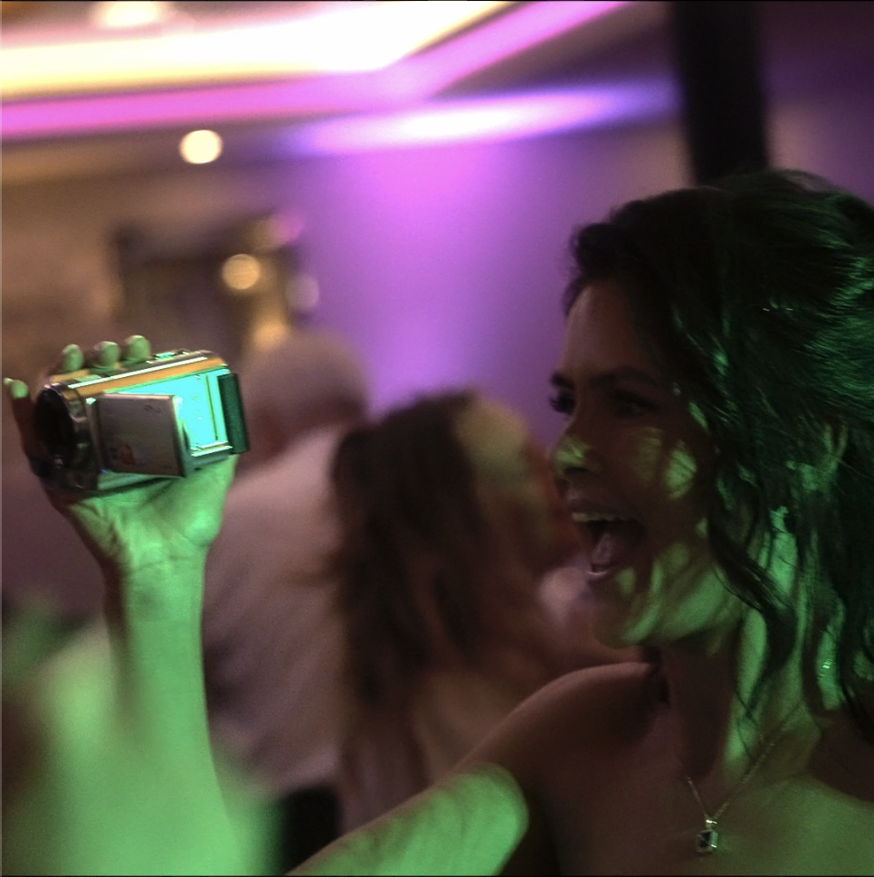 A previous Eye Flower Films client who opted for vintage camcorder footage with her videography package who is using it in the photo on the dance floor of her wedding day in the evening party.