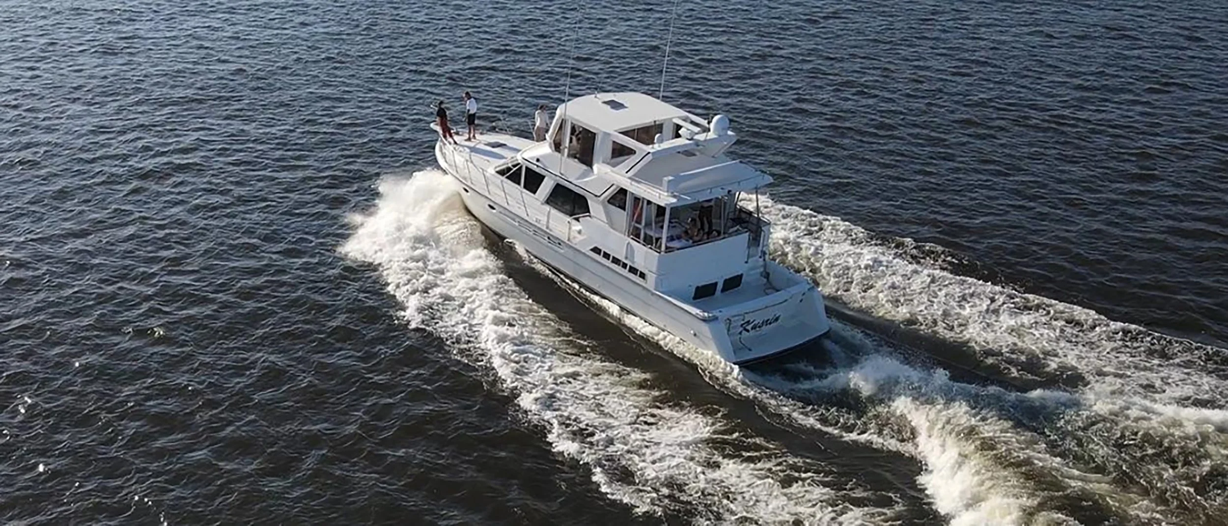A white yacht moving through the water with four people on board.
