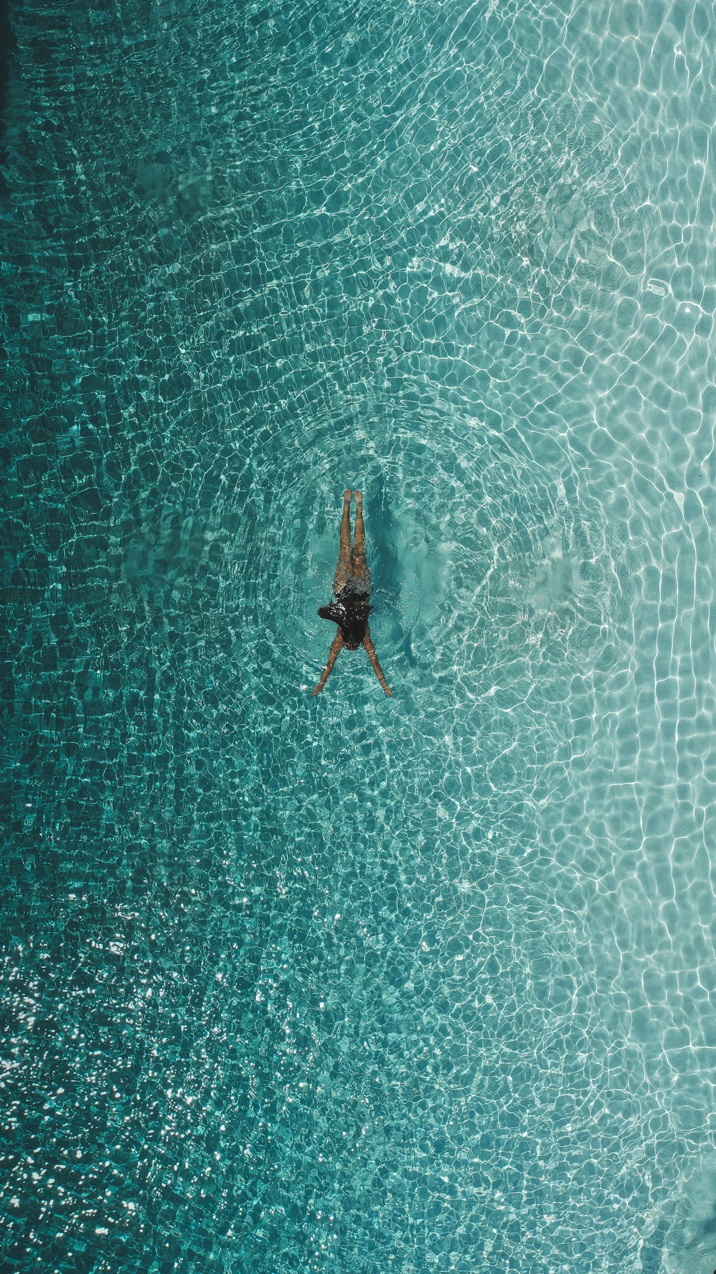 A person swimming in a clear, blue swimming pool seen from above.