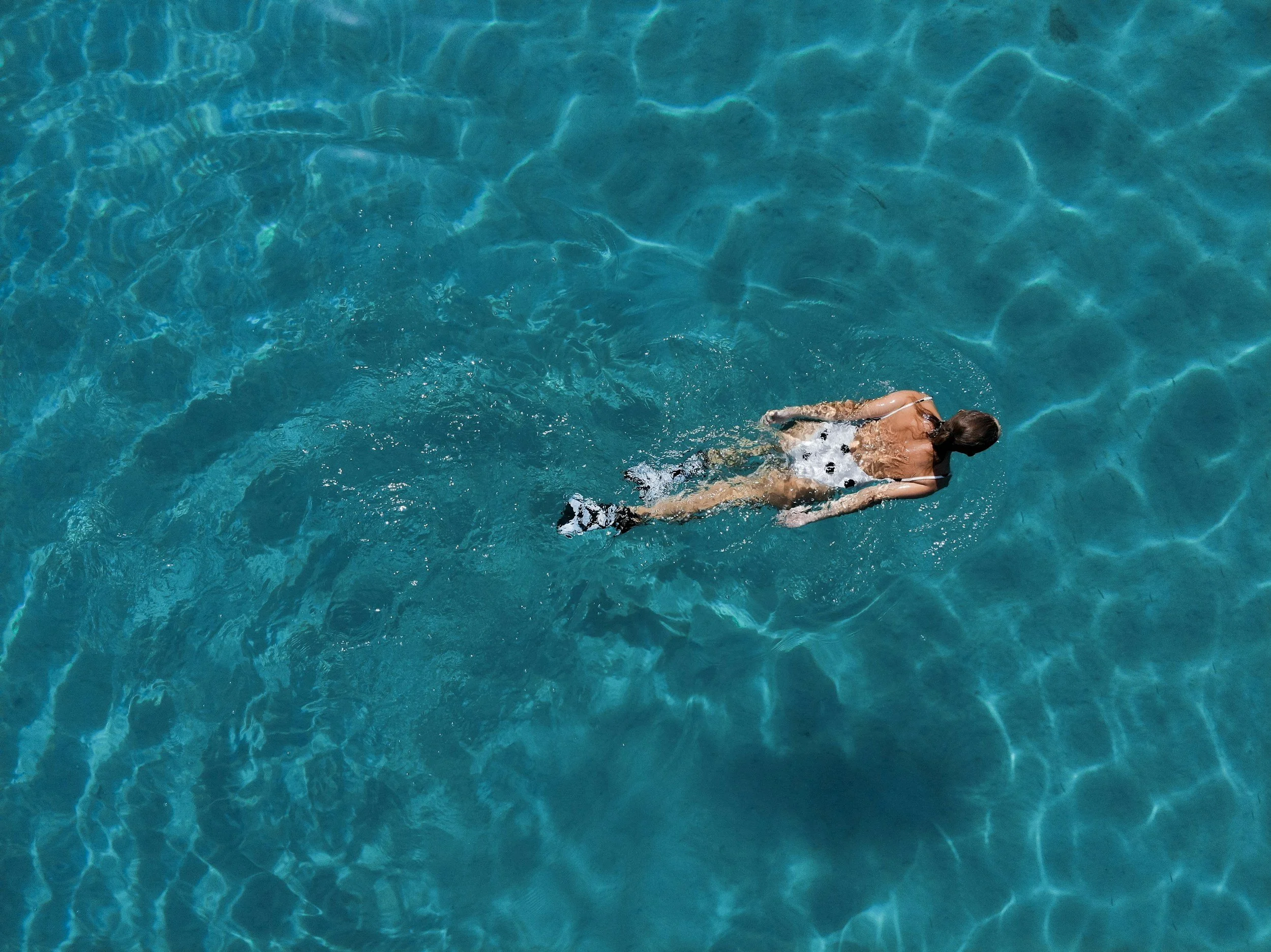 A woman swimming in a clear blue swimming pool, viewed from above.