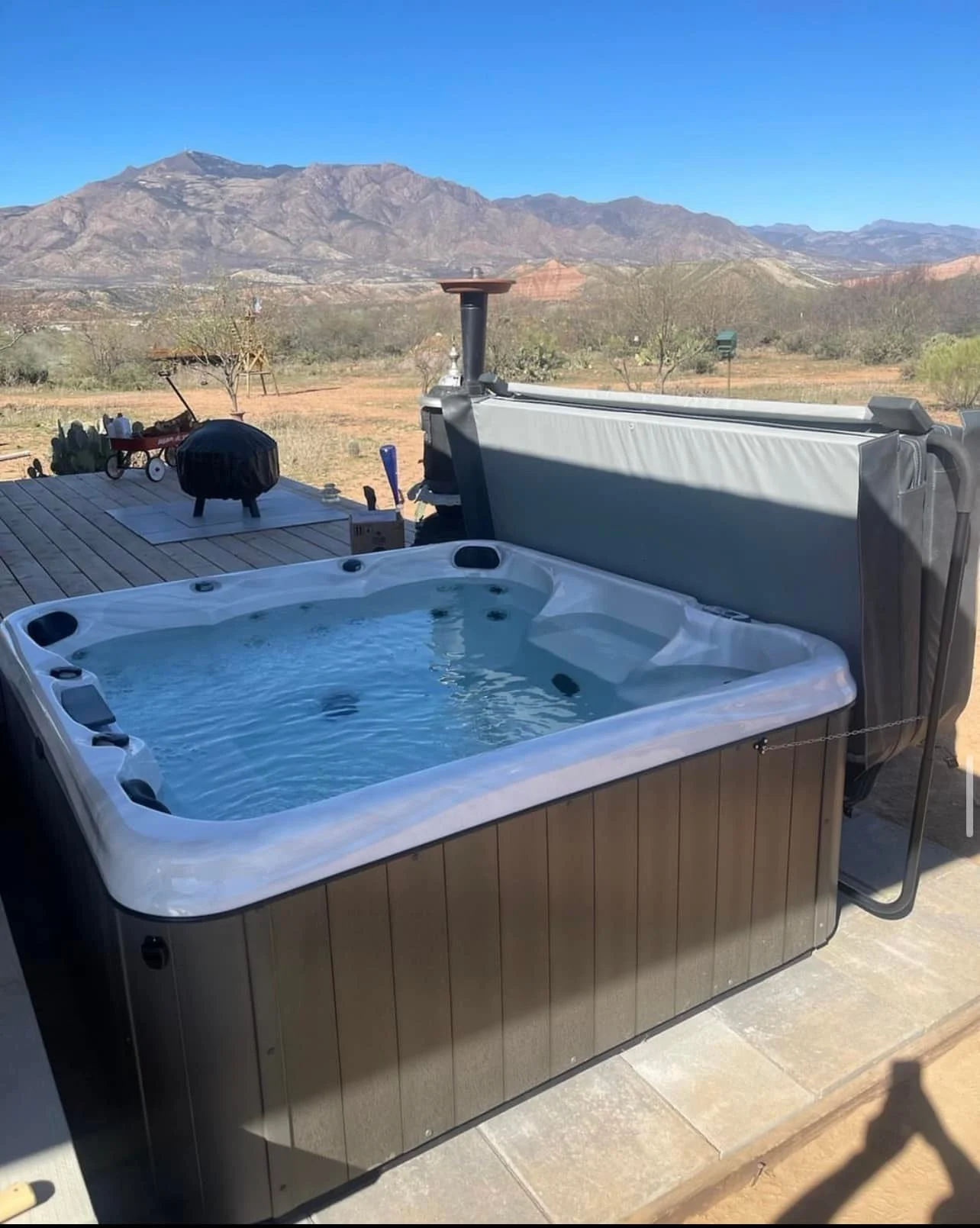 Outdoor hot tub on a patio overlooking a desert landscape with mountains in the distance under a clear blue sky.